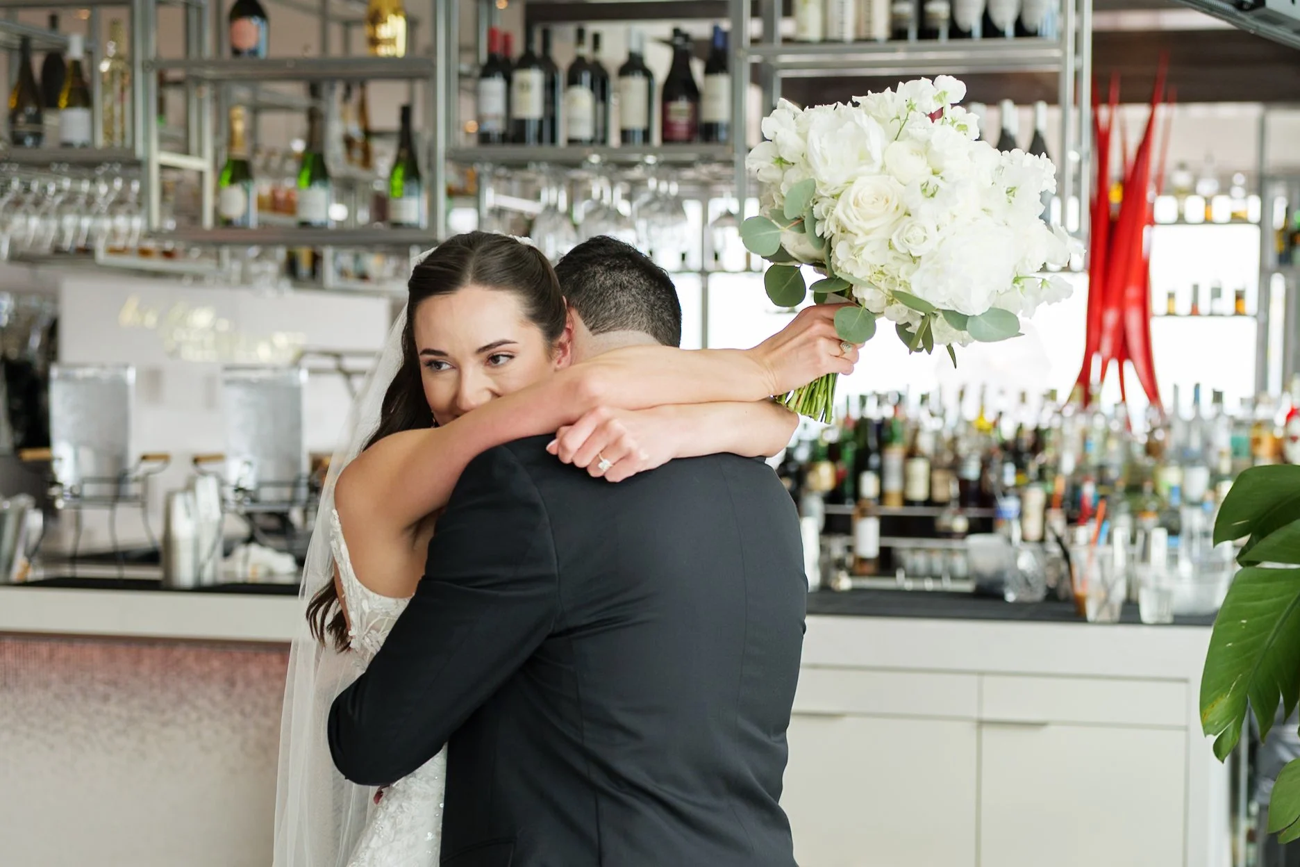 A bride and groom embrace, with the bride holding a bouquet of white flowers, in the rooftop bar at Nuvole Rooftop in Uptown, Charlotte.