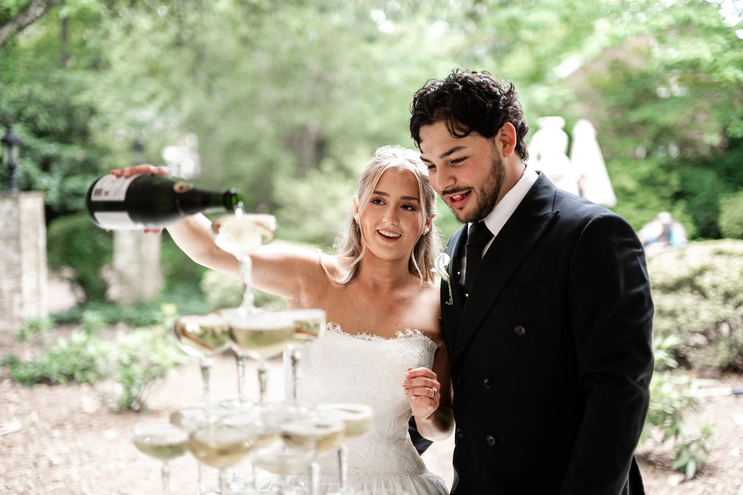 A bride and groom at a wedding reception outdoors at The Morehead Inn located in Charlotte, NC, pouring wine into a tower of glasses.