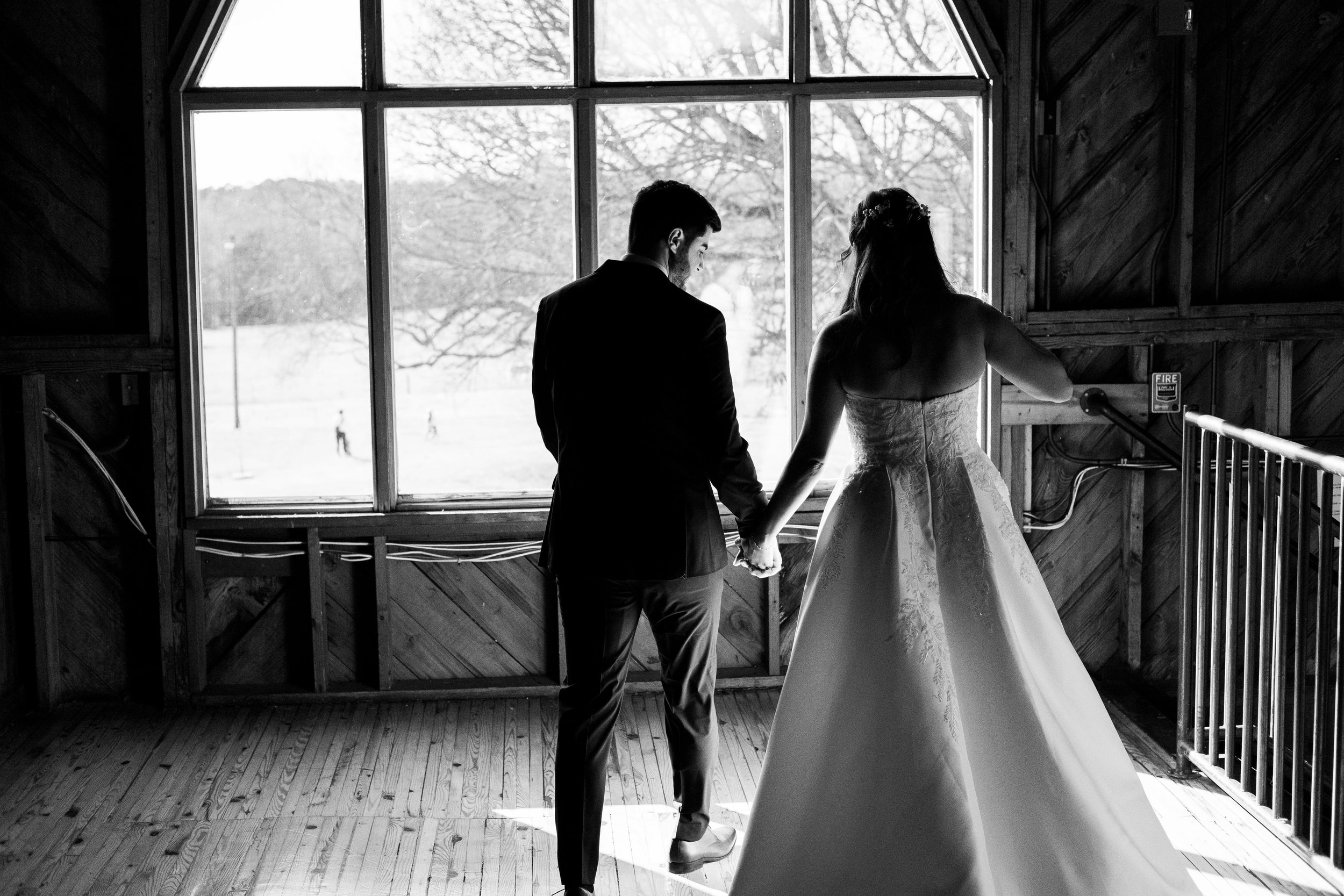bride and groom holding hands in front of big barn window in upstairs loft at Founders Dairy Barn