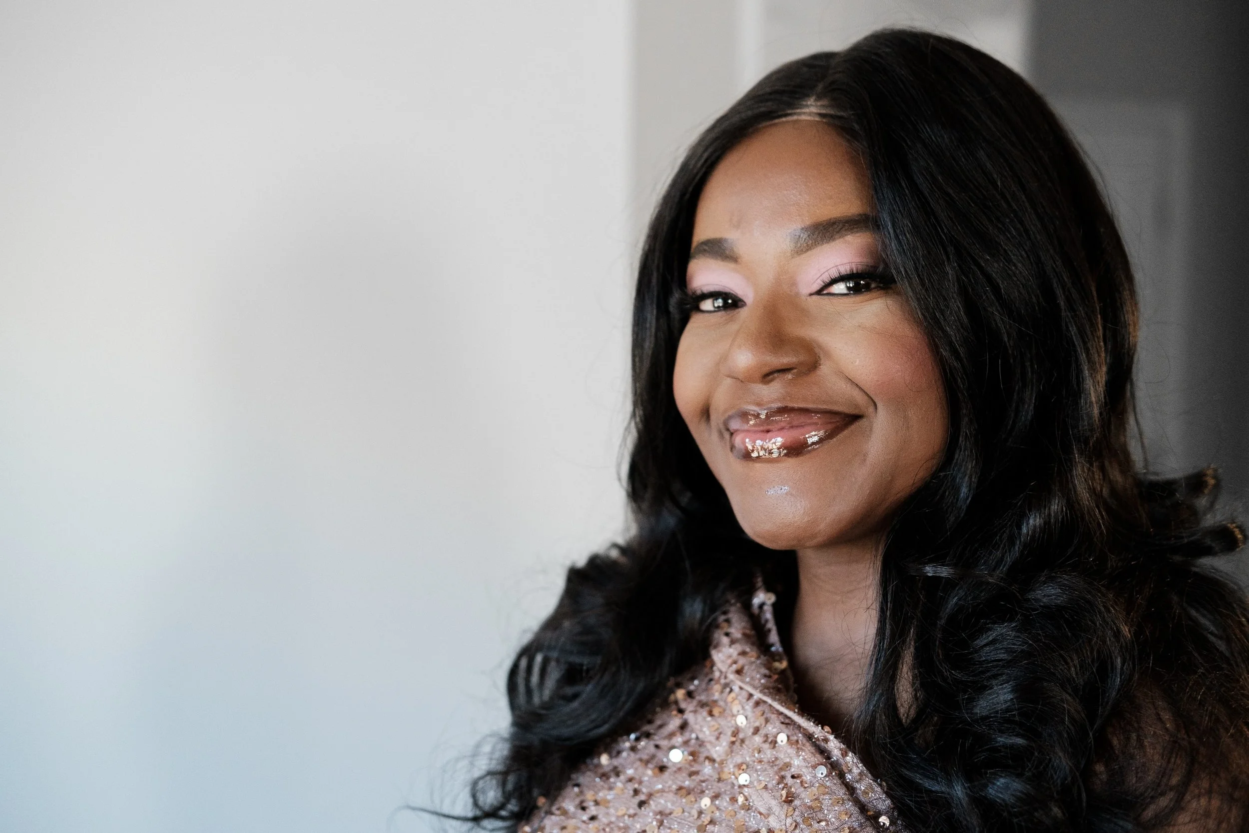 Close-up portrait of a woman with long black wavy hair, smiling, wearing a sparkly light-colored top.
