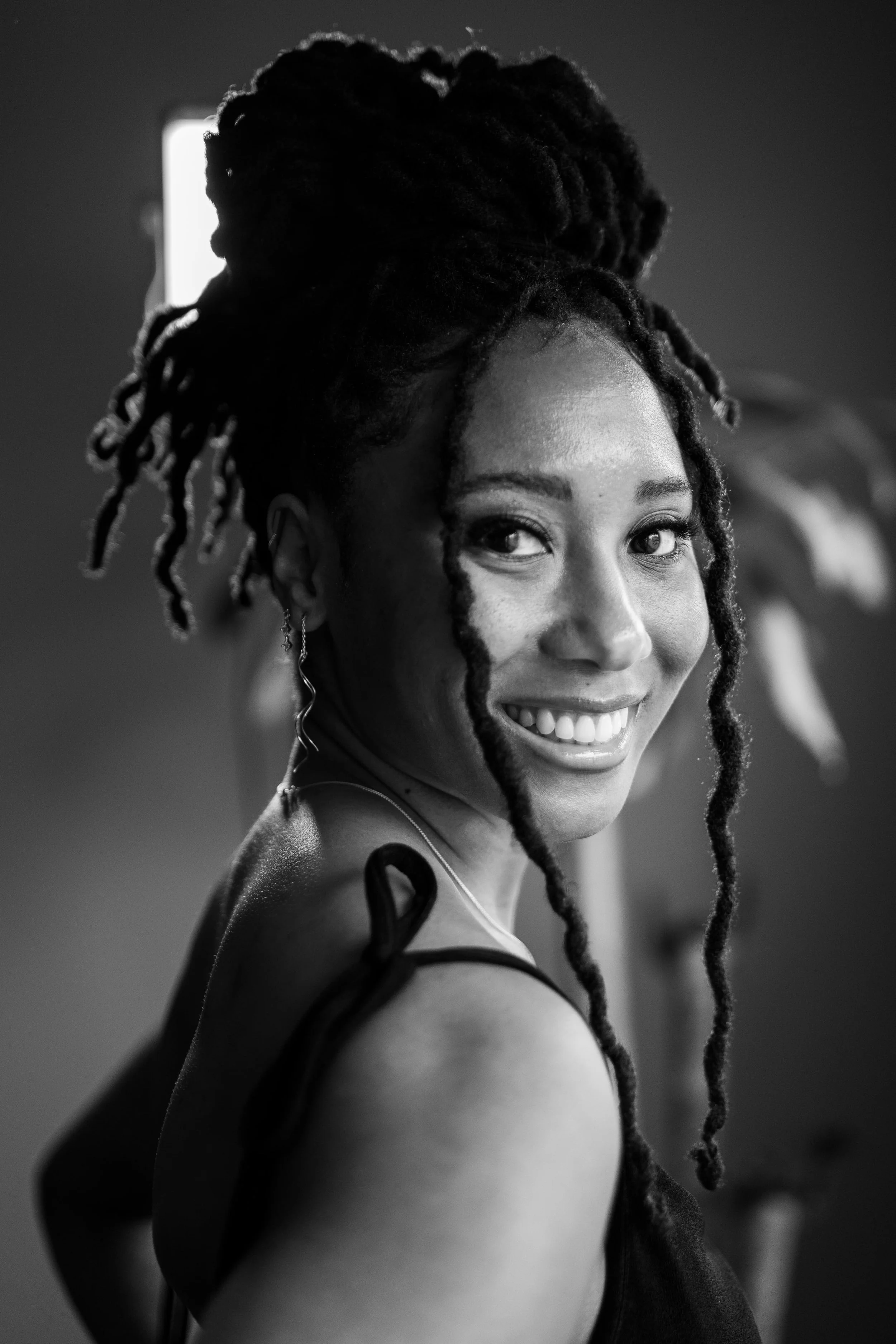 Black and white portrait of a woman with dreadlocks, smiling, looking at the camera.