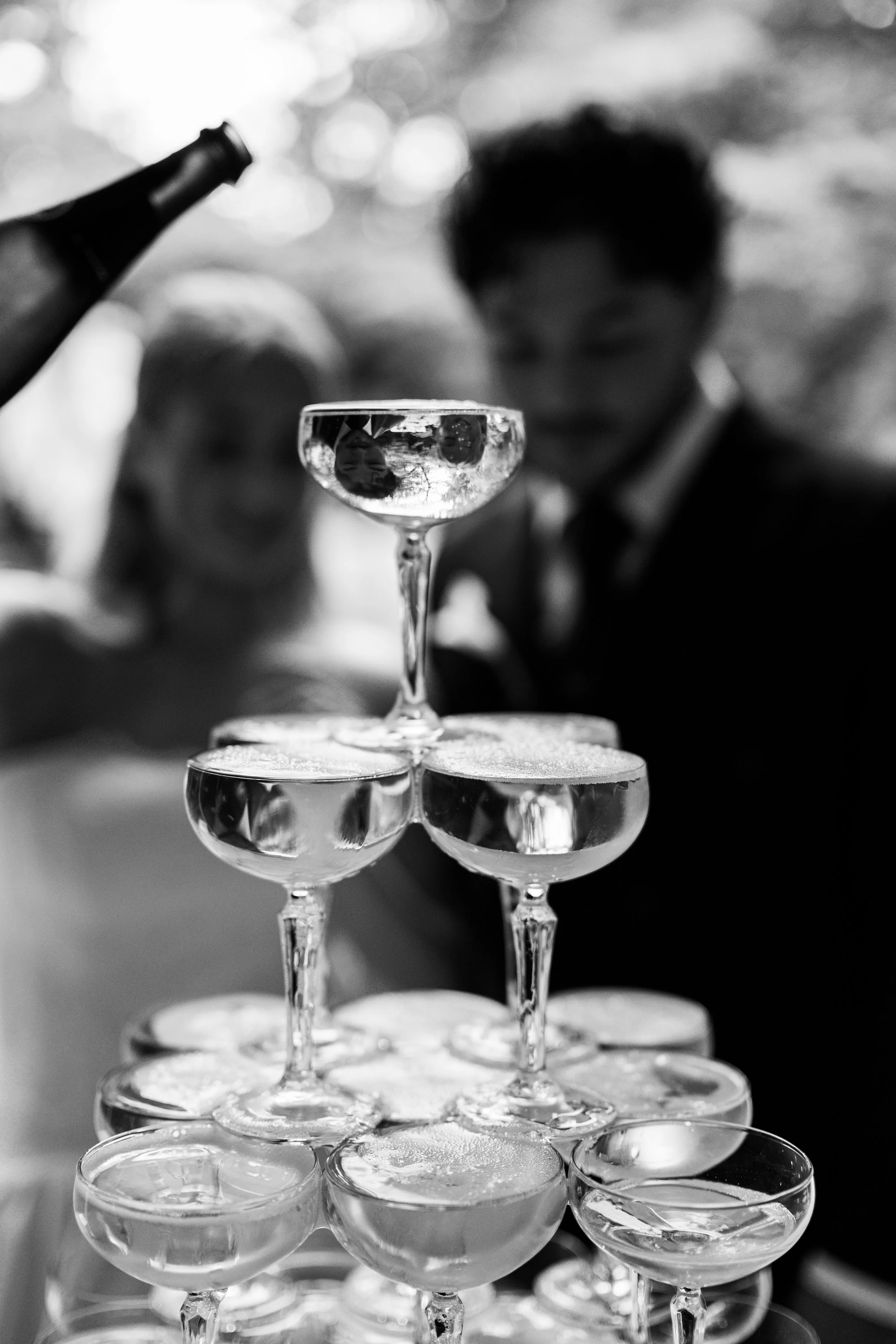 A person is seen through a stack of champagne glasses, with the glasses reflecting light and the person's face upside down at The Morehead Inn