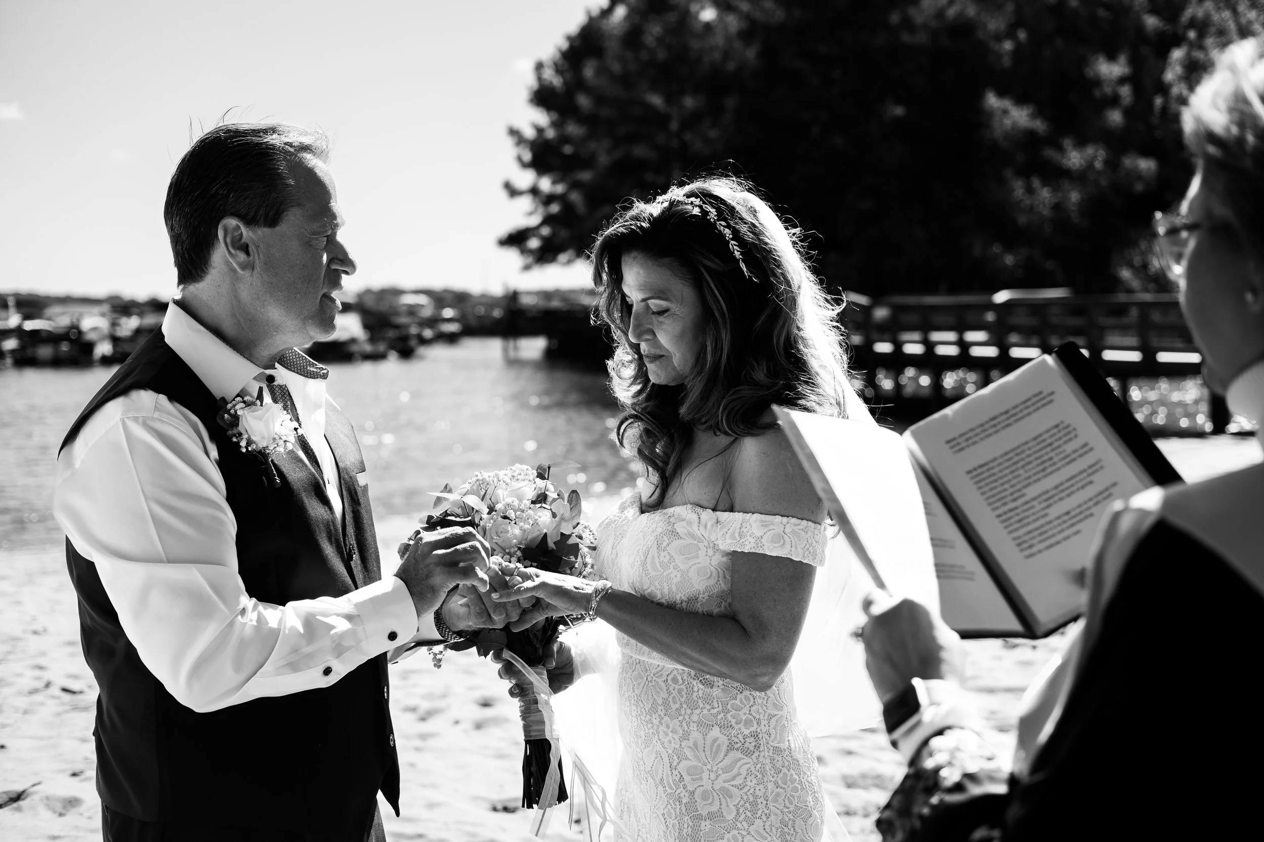 black and white photo of a groom placing ring on brides hand during a beach wedding at Lake Norman.