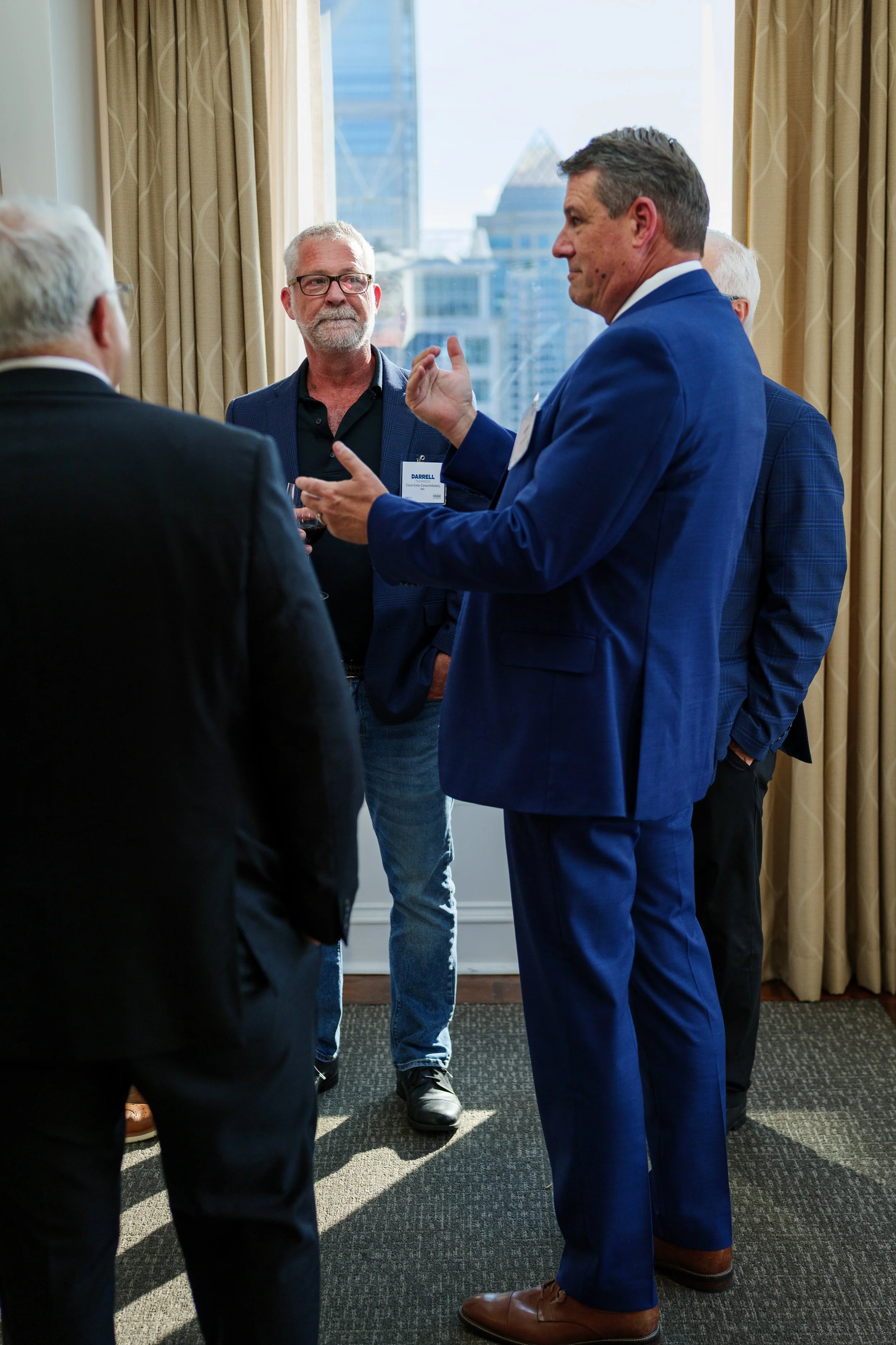Group of men engaged in conversation during a professional event in a high-rise office with city skyline view.