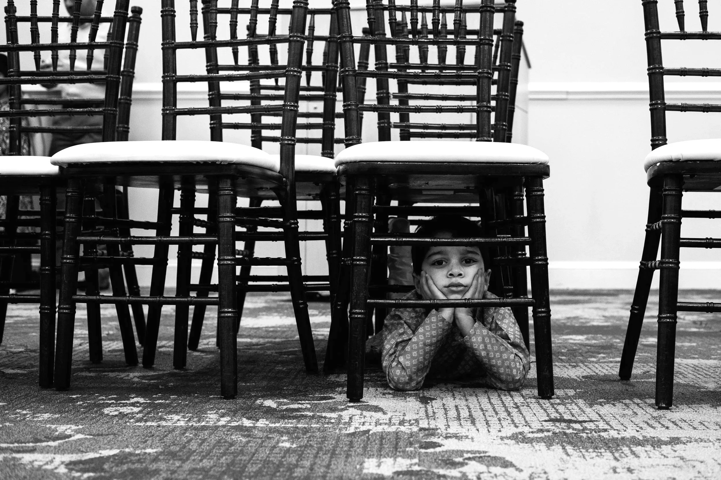black and white photo of you young buy laying under a chair, with both hands under his chin looking at the camera during a charlotte family session