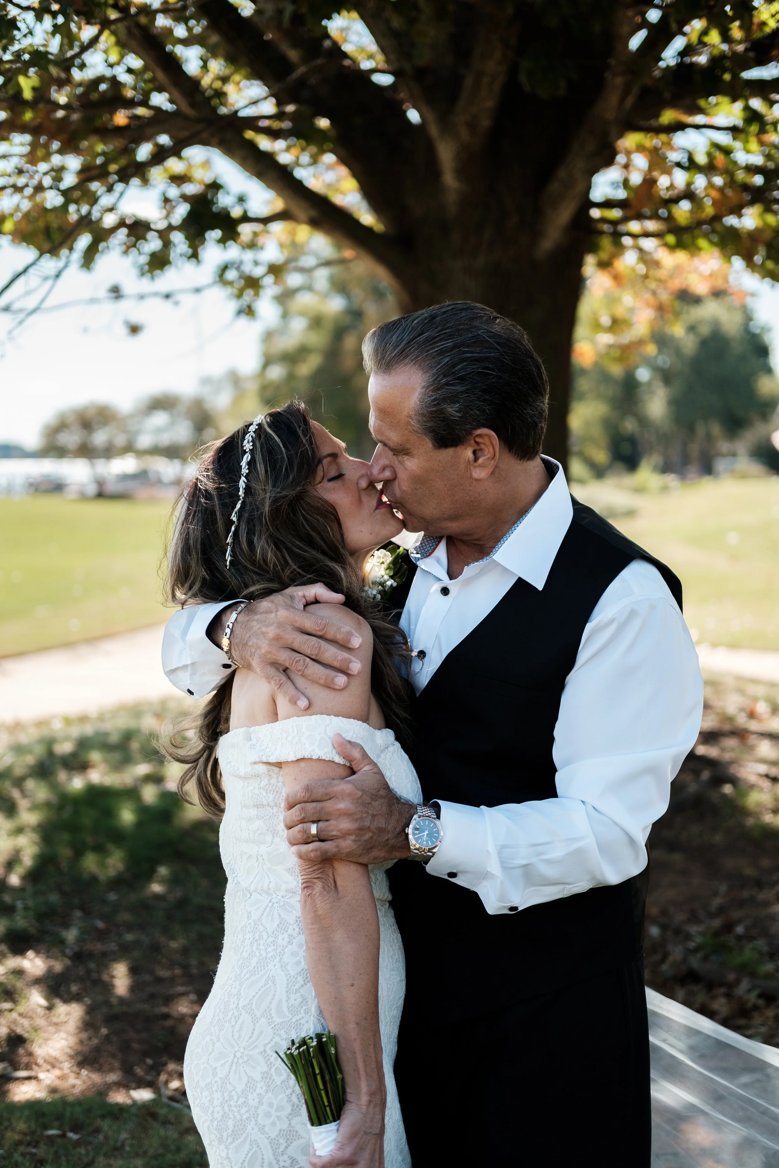 older bride and groom kissing under a tree.