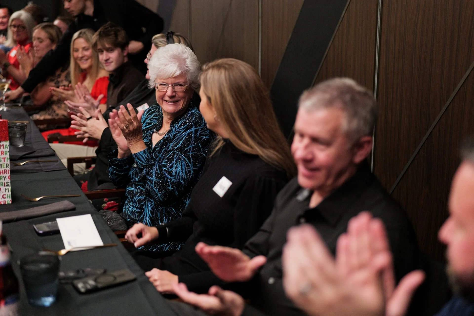 woman smiling and clapping while sitting beside her co-workers during a holiday work party in Charlotte, NC