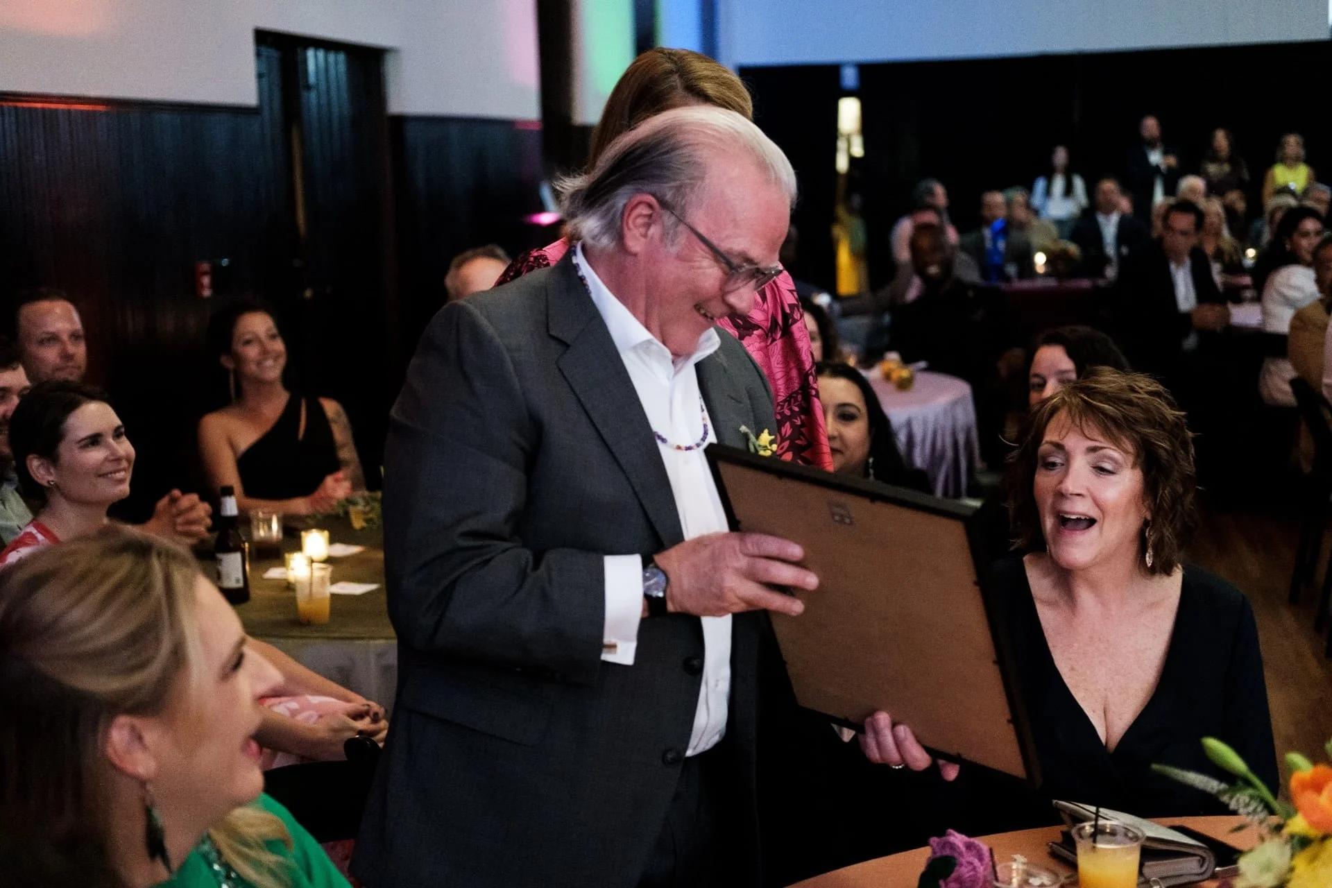 man smiling while holding a picture frame. He appears to be showing the picture to the guests seated around him during a charity event in Charlotte