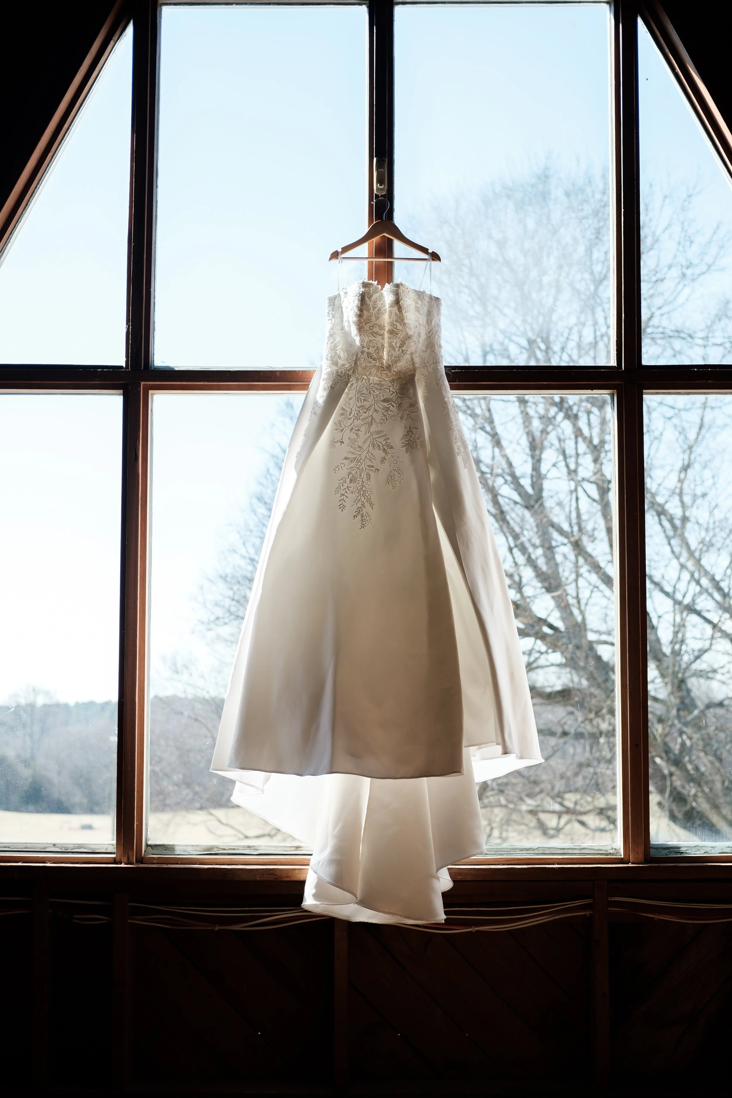 photo of a wedding dress hanging in a barn window in the upstairs loft of Founders Dairy Barn. Photo by Brandon Pickett Photography