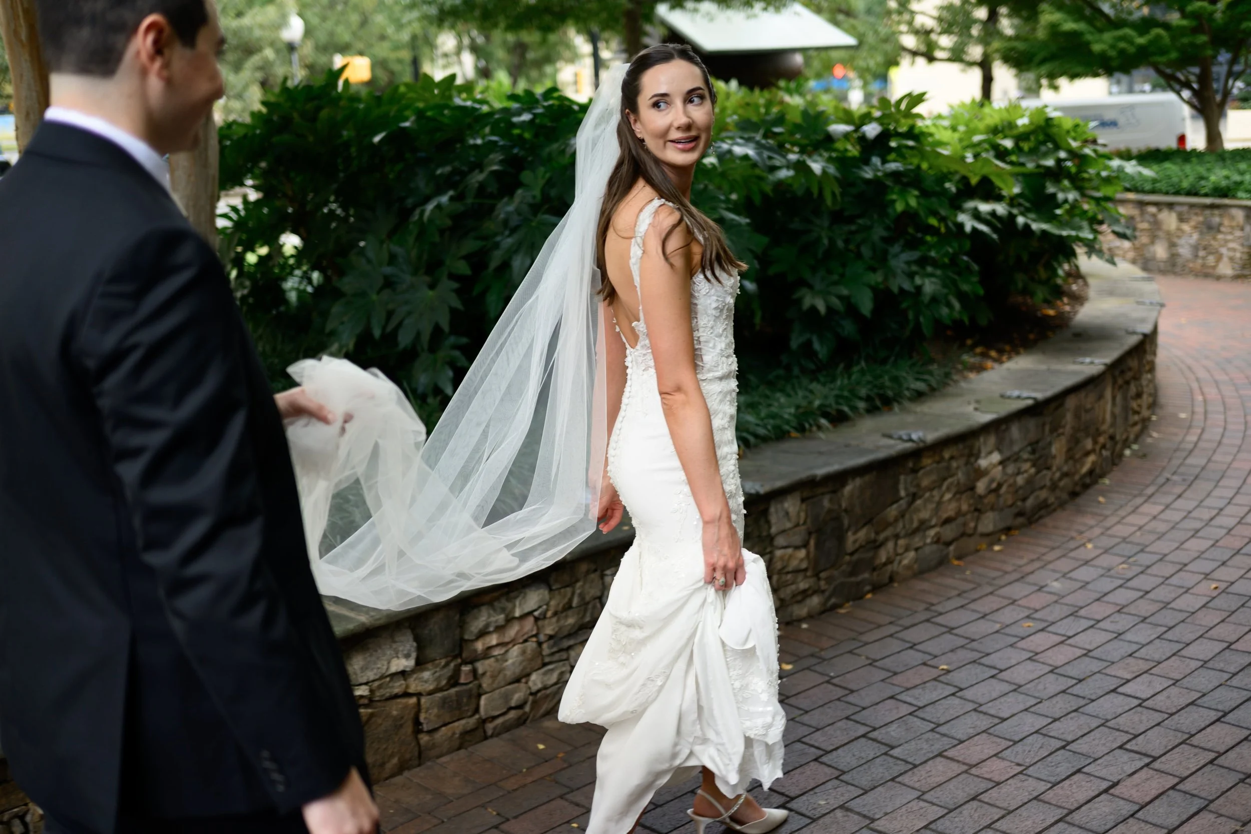 Bride in wedding dress and vale walking and looking back at photographer at The Green in Charlotte, NC