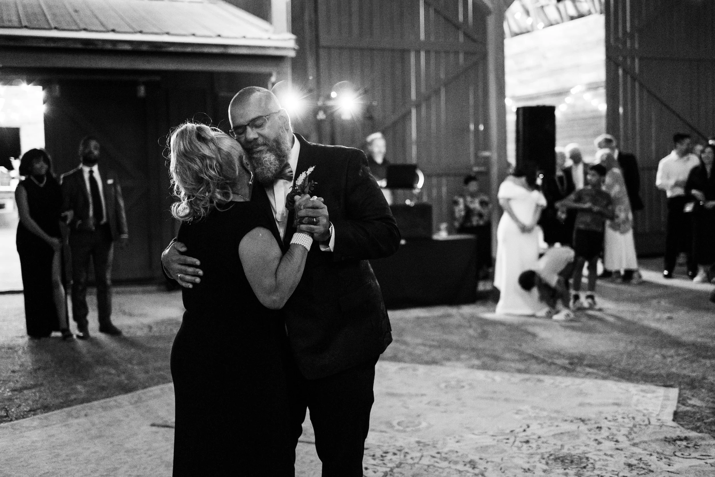 A groom and bride sharing their first dance at their wedding reception in a barn, with guests watching in the background at The 1932 Barn in Charlotte