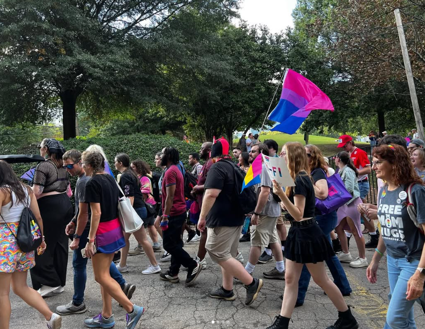 Side view of Bi+ GA marching through the park with bisexual pride accessories in Atlanta, GA