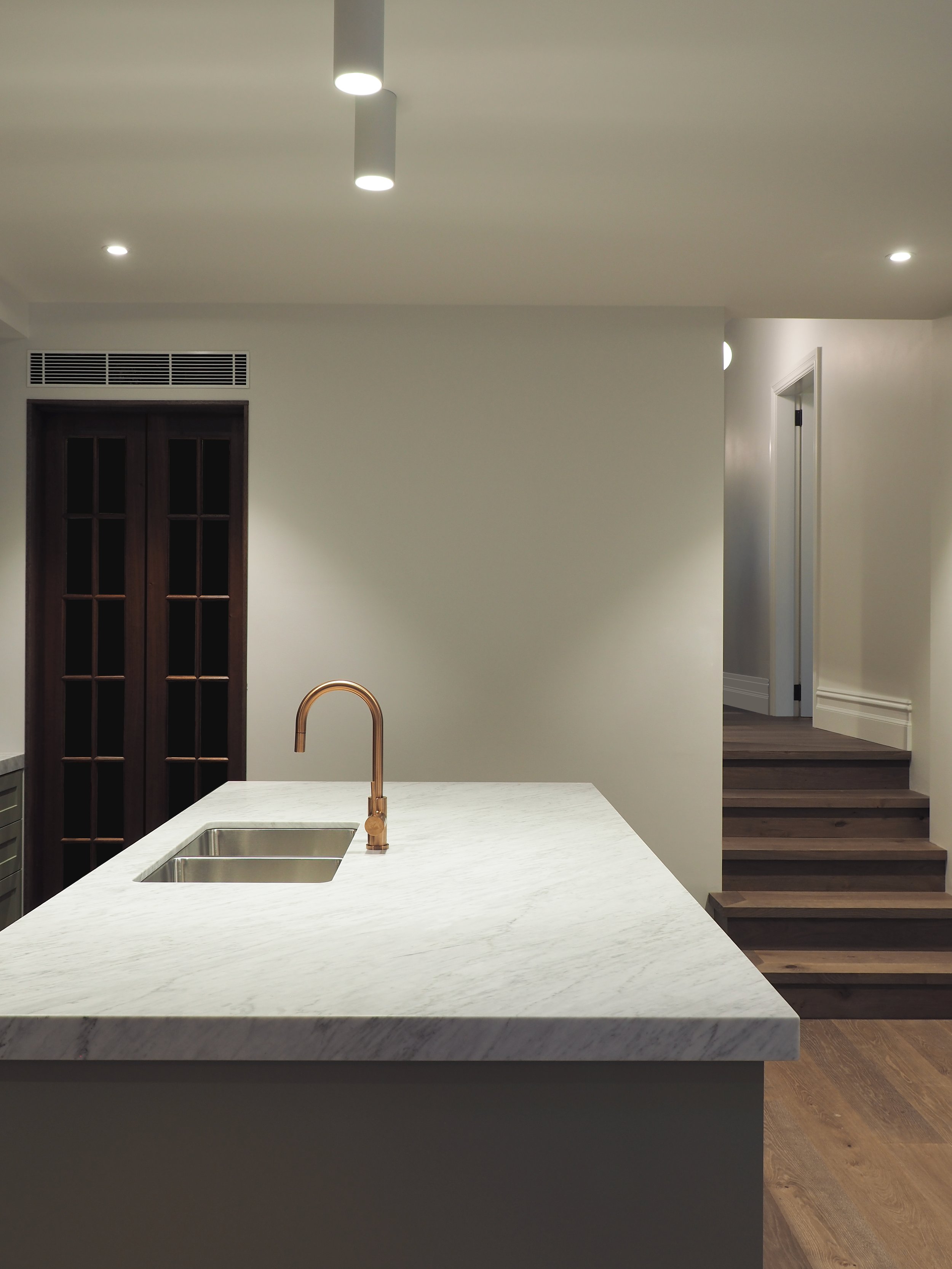 Modern kitchen with green cabinets, black subway tile backsplash, white marble countertop, and a copper faucet over a stainless steel sink.