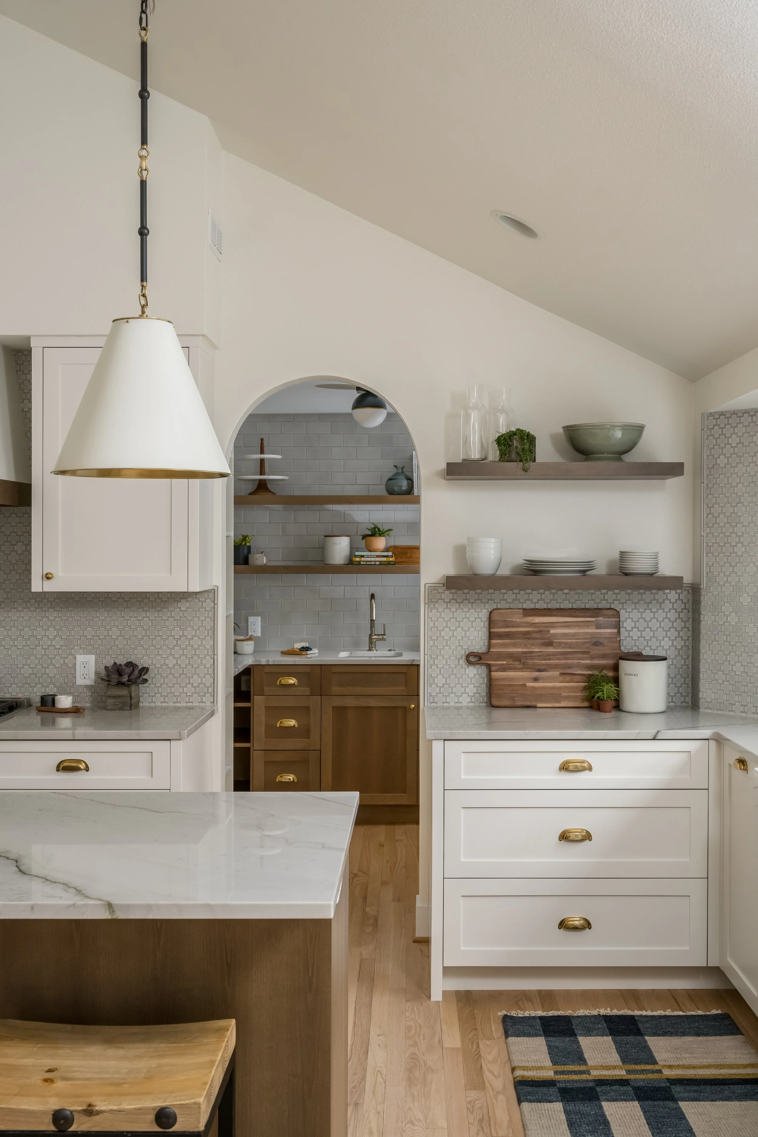 Warm modern kitchen remodel in Portland, Oregon with white cabinetry, brass hardware, marble countertops, and arched butler’s pantry.