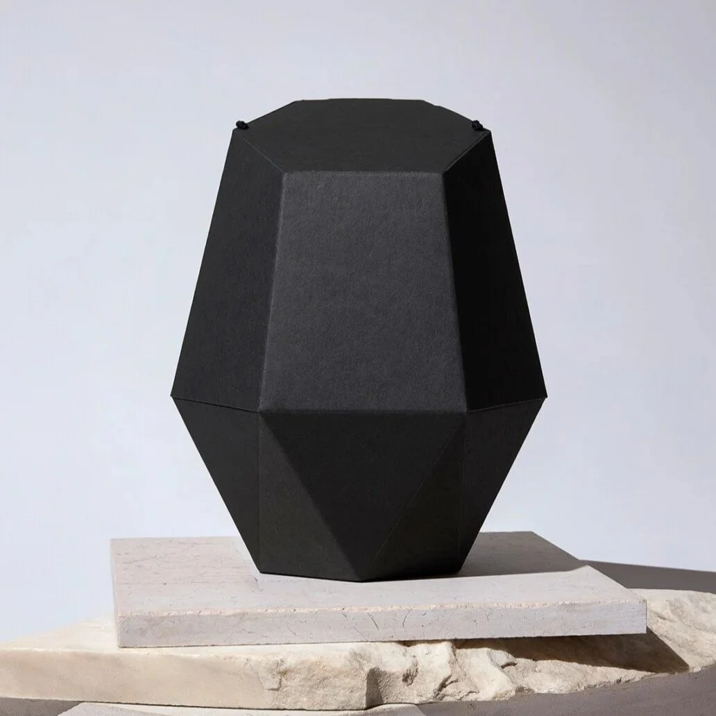 Schwarze geometrische Papierurne auf einem weißen Podest.