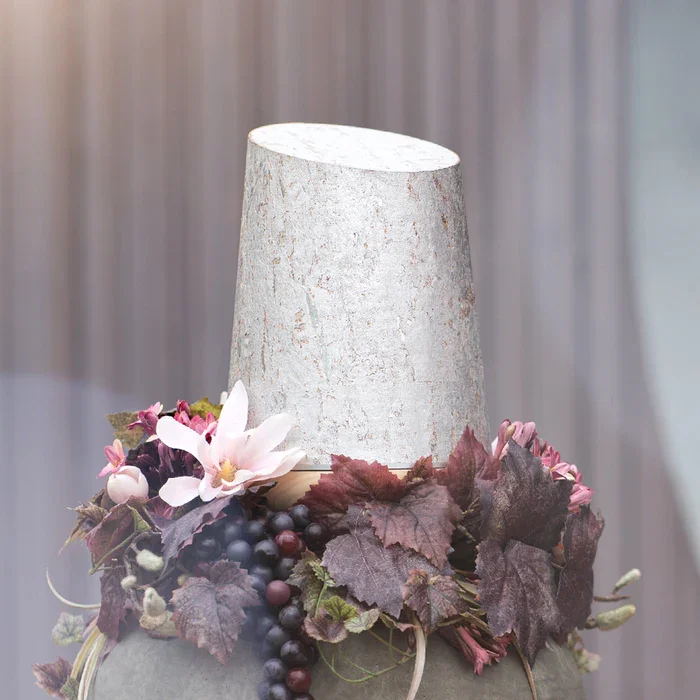 Eine Urne aus silbrigem Kork umgeben von Dekorationsblumen und Blättern.