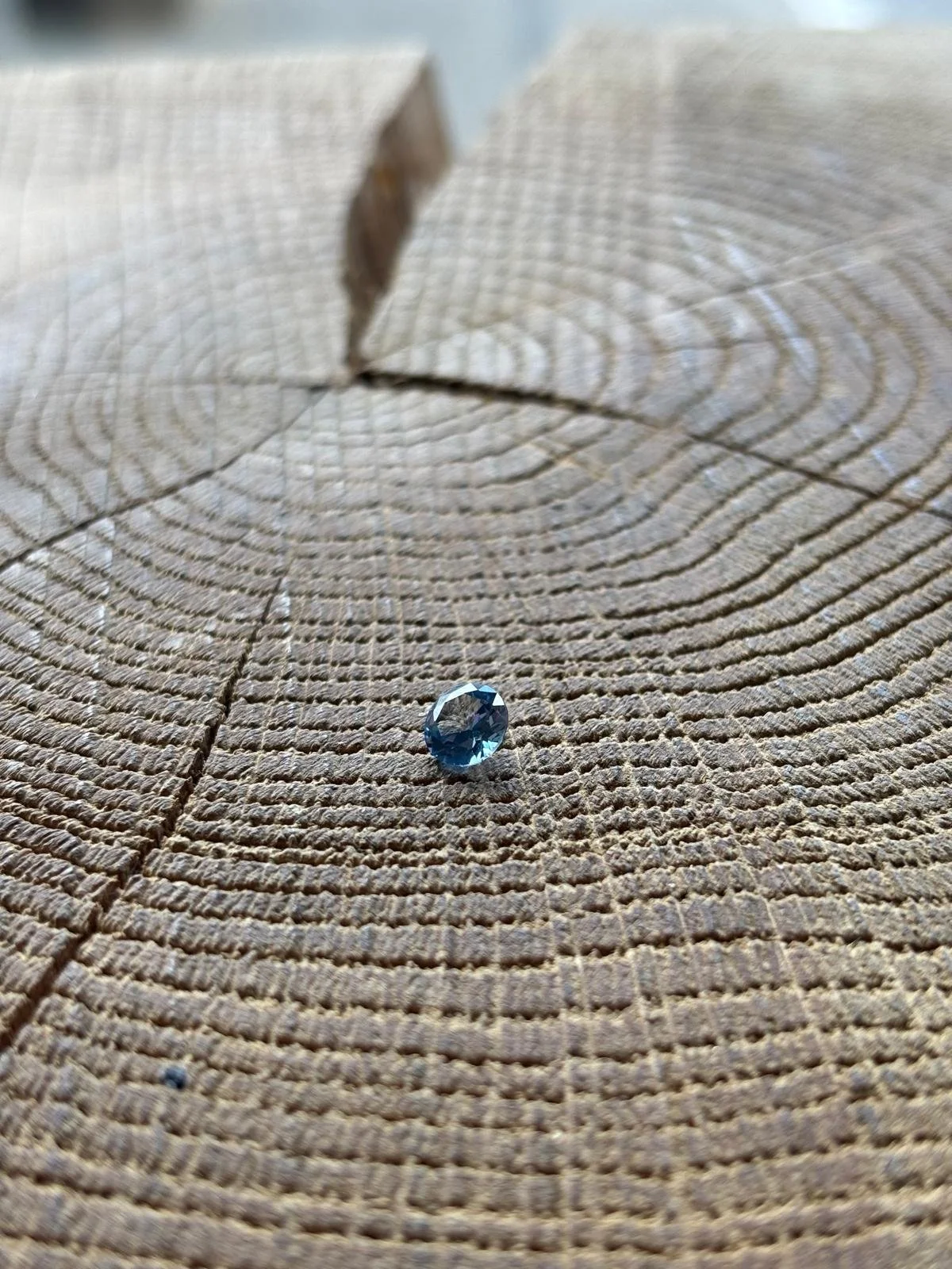 Ein blauer, facettierter Edelstein liegt auf einer Holzscheibe mit sichtbaren Jahresringen. Diamant aus Kohlenstoff. Erinnerungsdiamant Algordanza. Haare und Asche.
