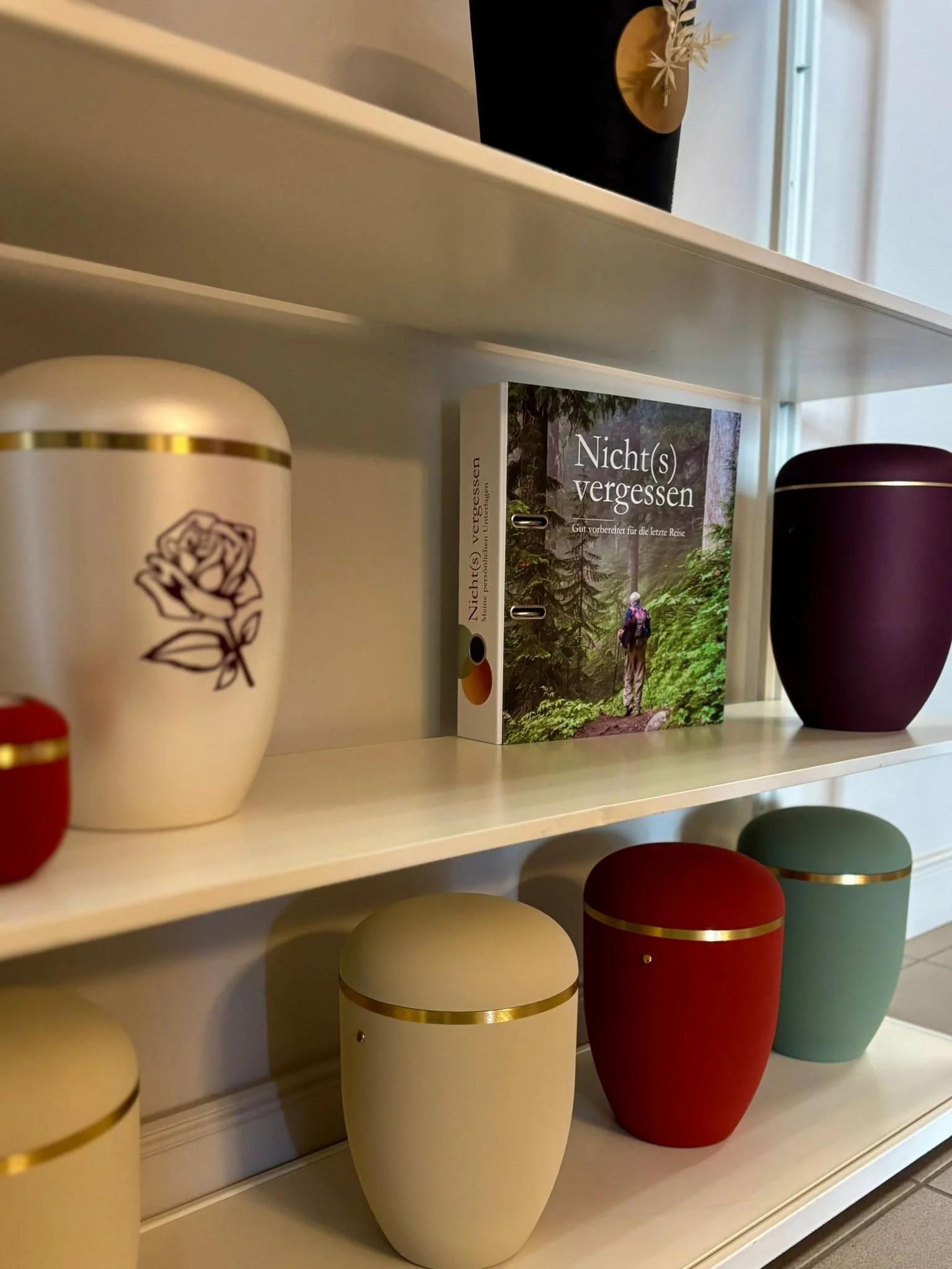 Bücherregal mit mit bunten Urnen und einem Buch namens Nicht(s) Vergessen.