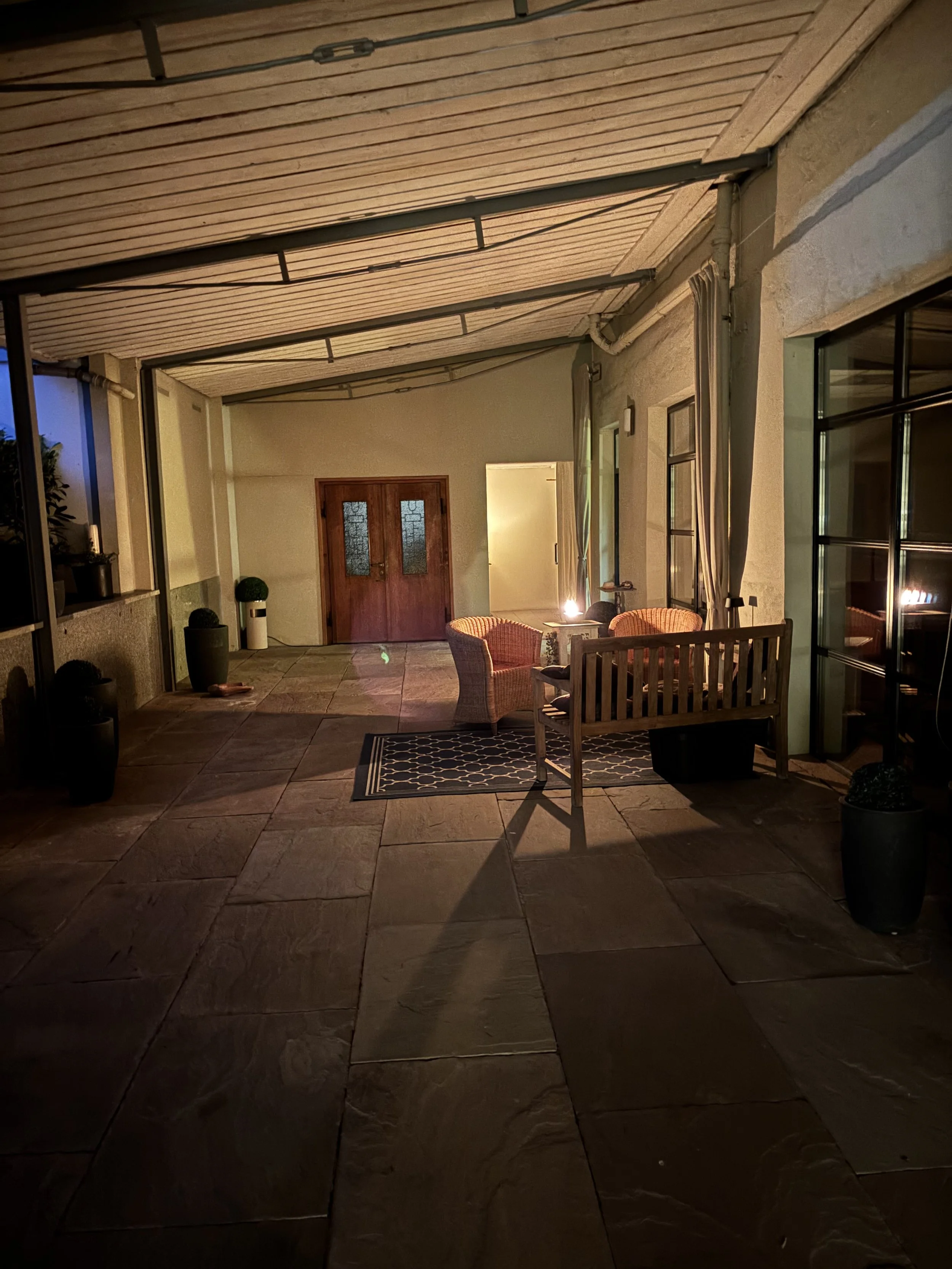 Gemütlicher Balkon bei Nacht mit Sesseln, Tisch und Lichterkette, umgeben von Pflanzen in Töpfen.