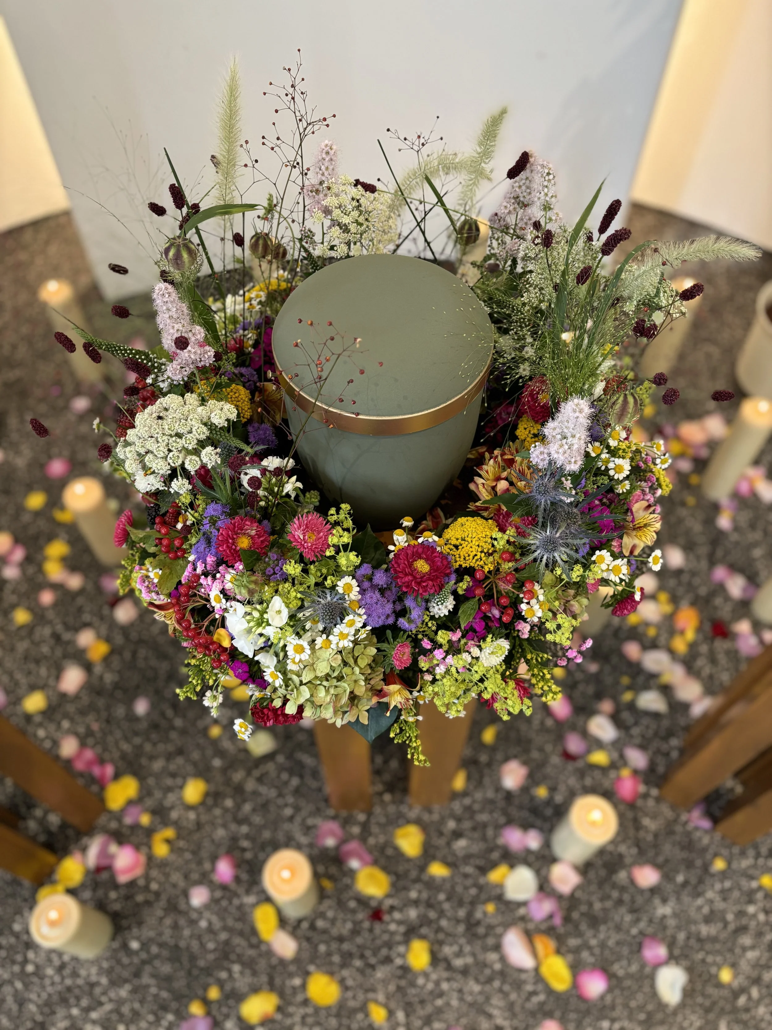 Blumenkranz mit bunten Blumen und Kerzen auf einem Boden mit Blumenblättern