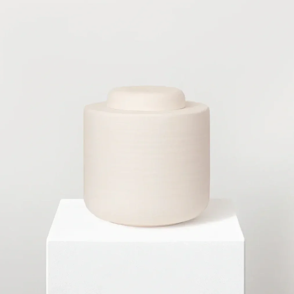 Ein minimalistischer weißen Keramikurne auf einem weißen Podest, im Hintergrund eine helle, neutrale Wand.