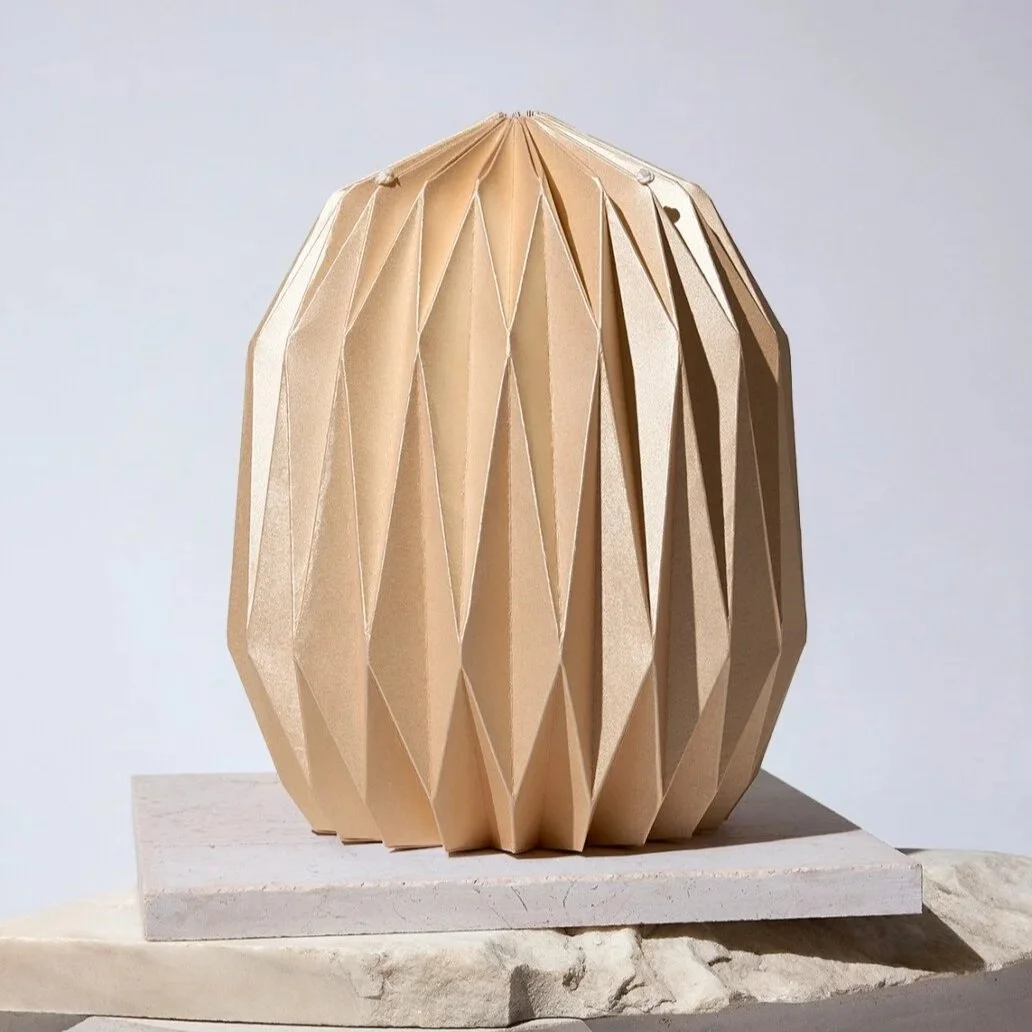 beige kunstvoll gefaltete Papierurne geometrischem Muster auf einem Stein