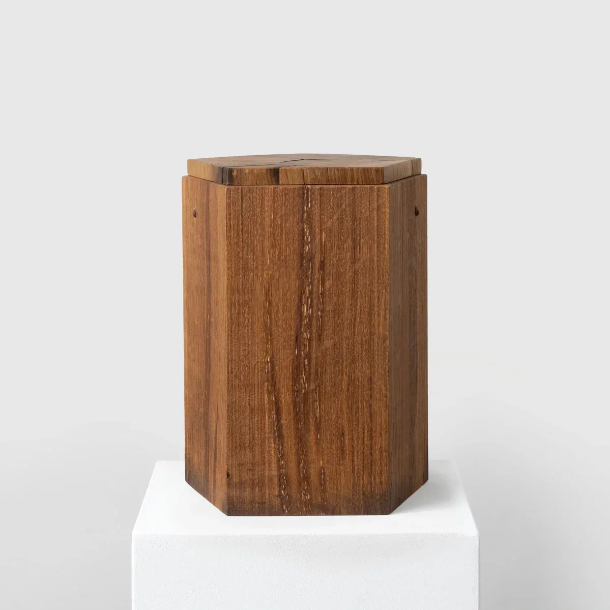 Eine Urne aus dunklem kostbarem Holz auf einem weißen Sockel, hervorgehoben vor einem hellgrauen Hintergrund.