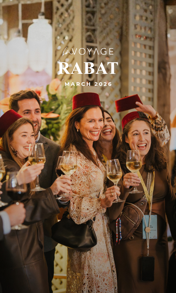 Three women smiling and standing together at an event in Rabat, March 2026, with two wearing red fez hats, one in a black blazer, another in a leopard print outfit, and the third in a black blazer over a maroon top, indoors with warm lighting.