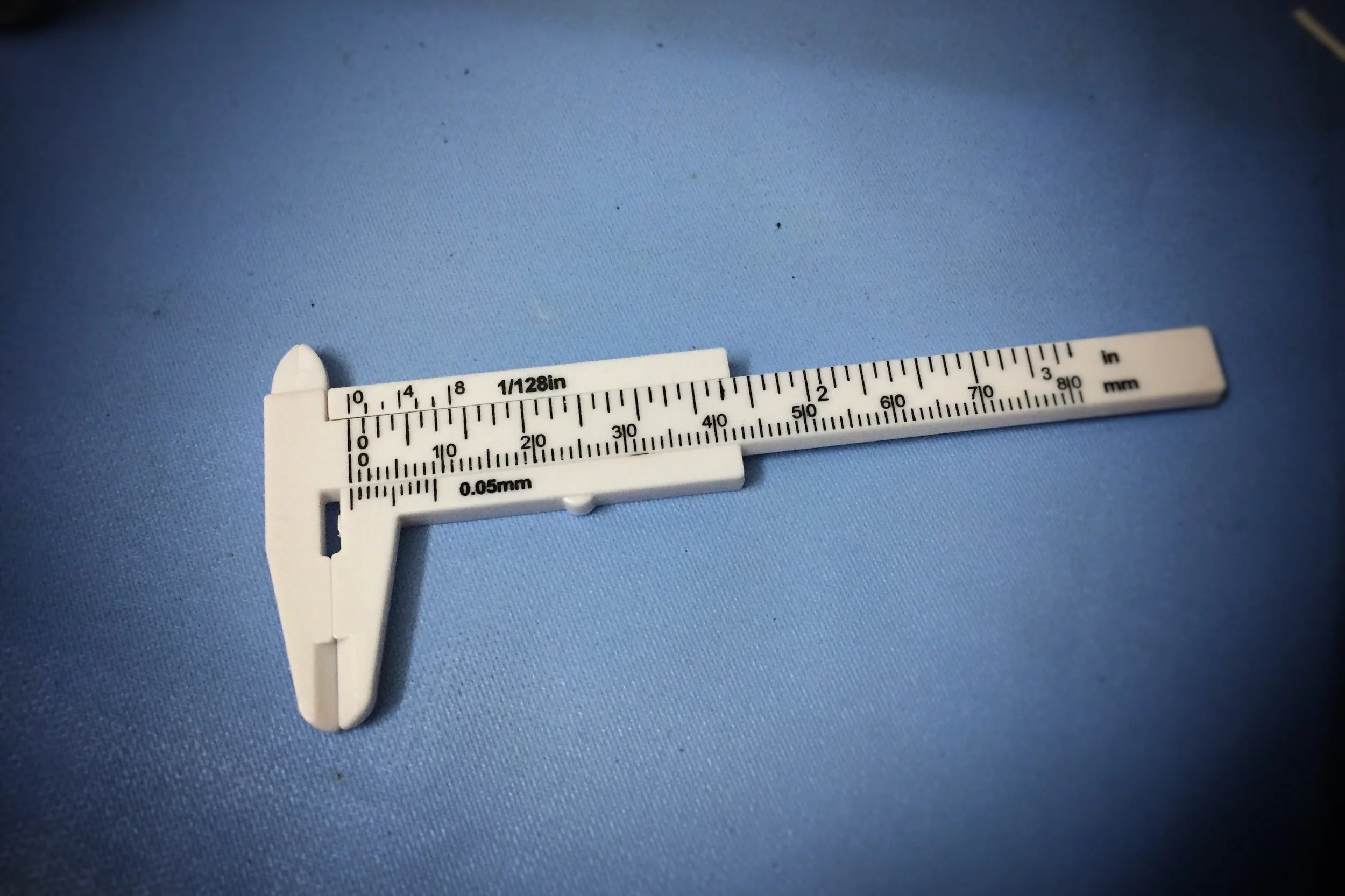 White plastic caliper on a blue background, marked with both inch and millimeter scales.