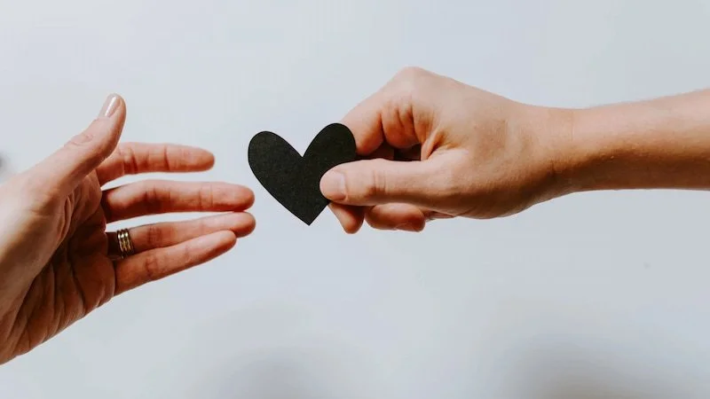 One hand reaching our for a black heart