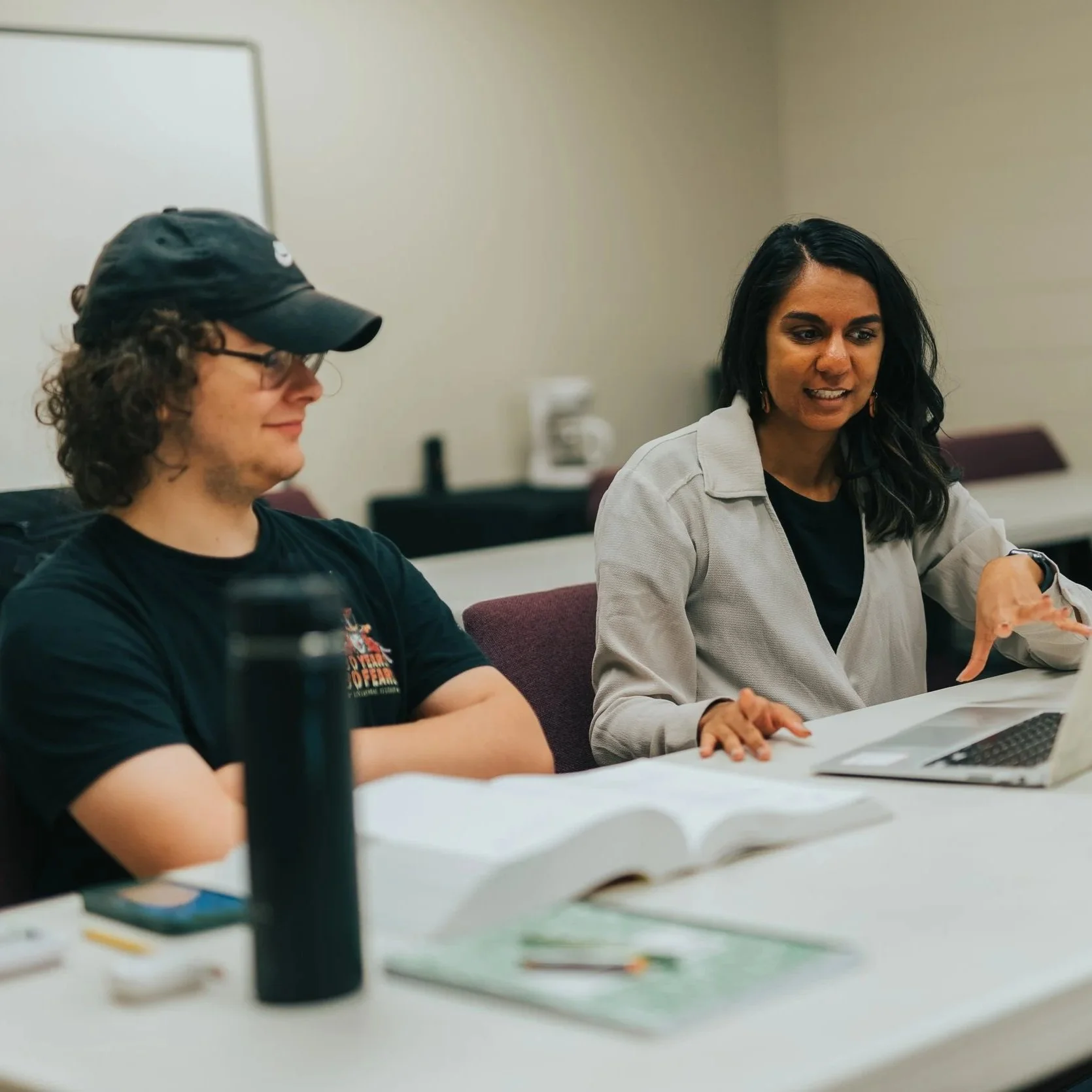 A Test Prep Coach sitting next to a student pointing to a laptop. There is an ACT prep book and learning materials on the table in front of them.