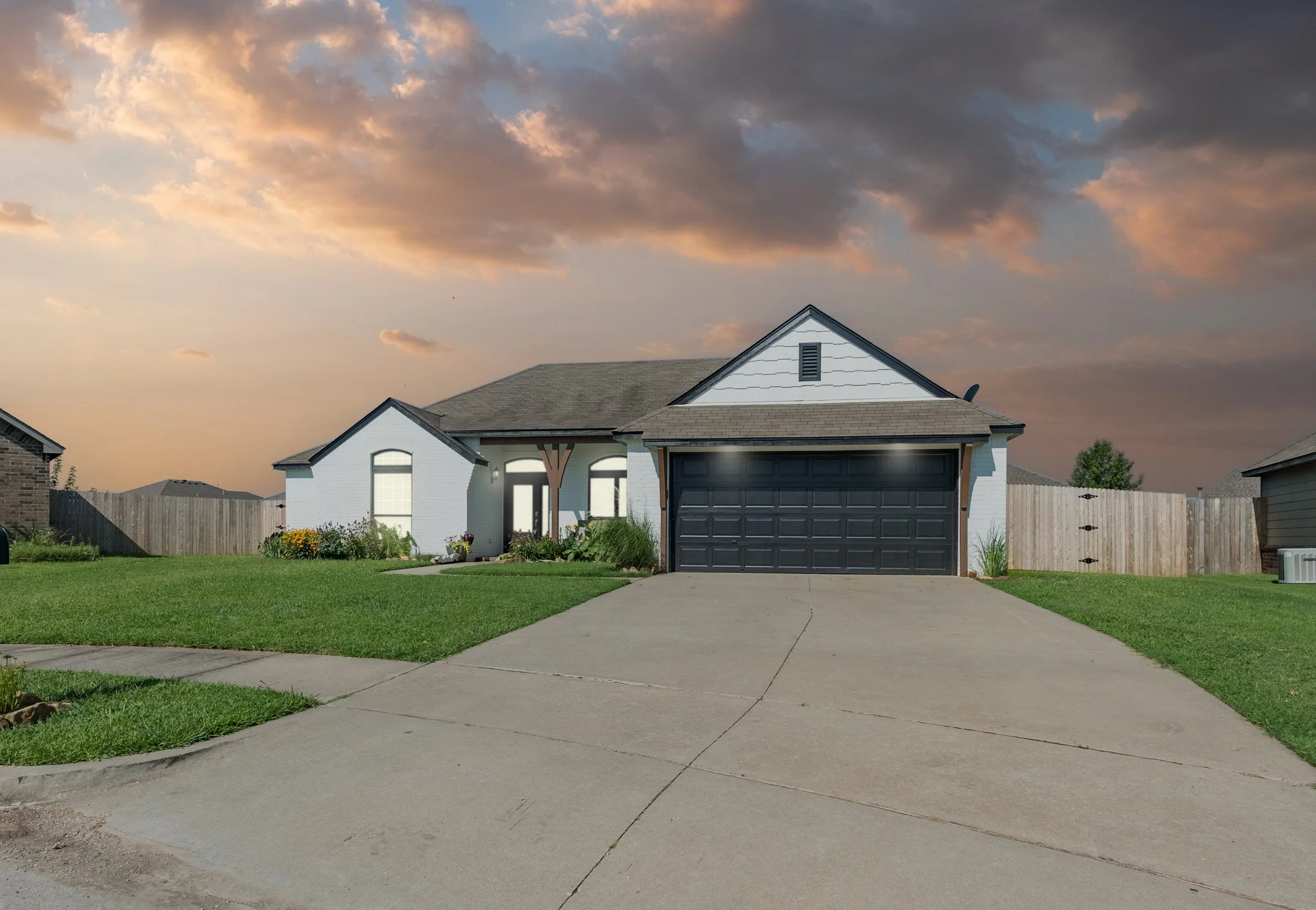 Photo of a white ranch style home with a black garage at sunset
