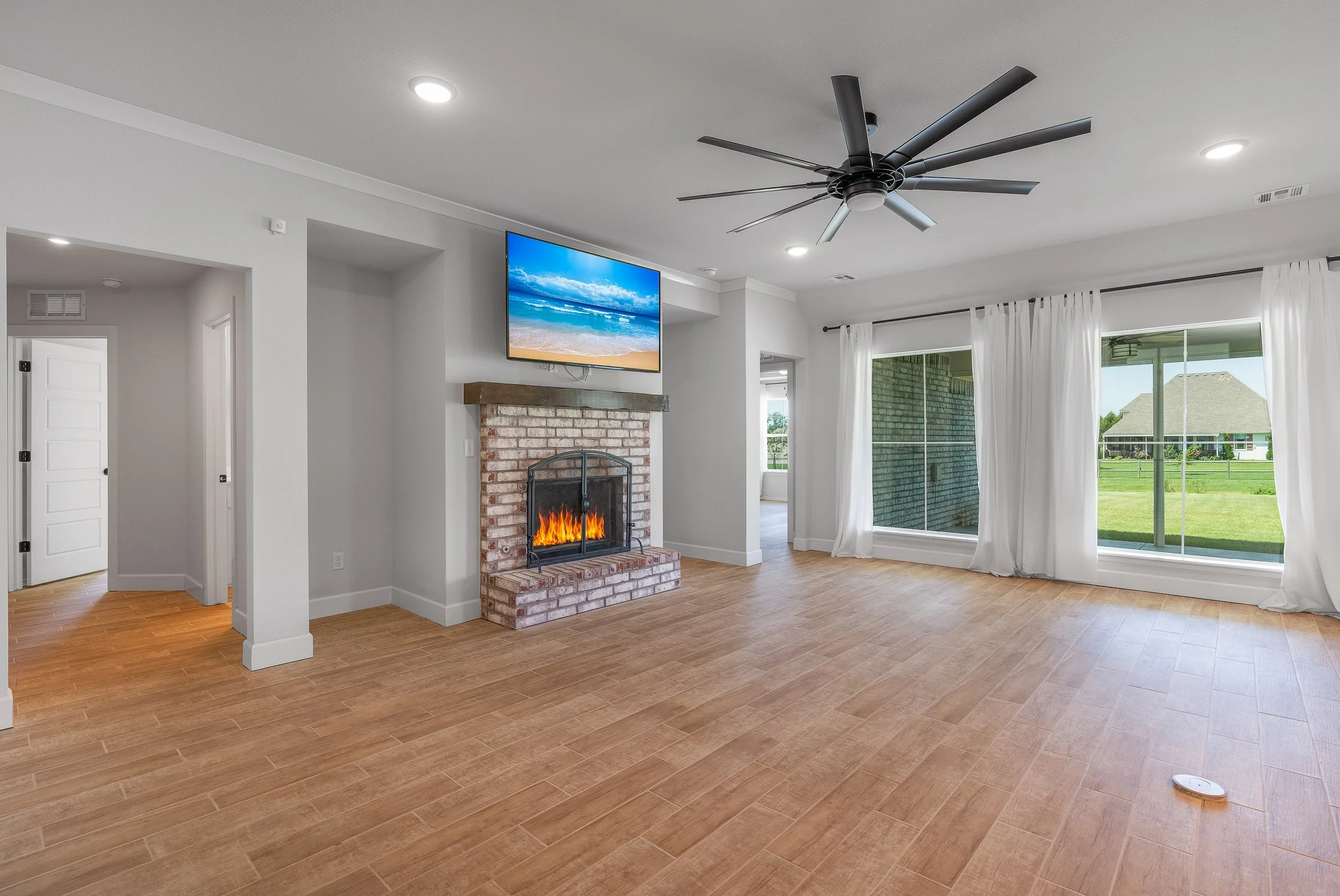 Large open white colored living room with a brick fireplace and large TV above it
