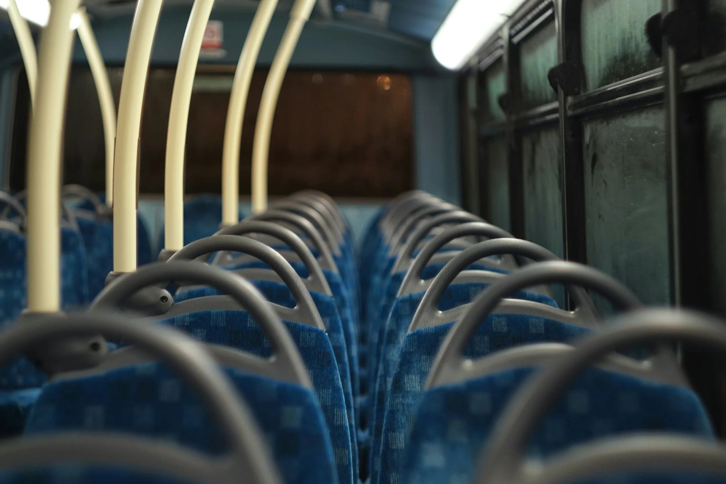 Interior view of a public bus with rows of empty blue seats and vertical handrails.