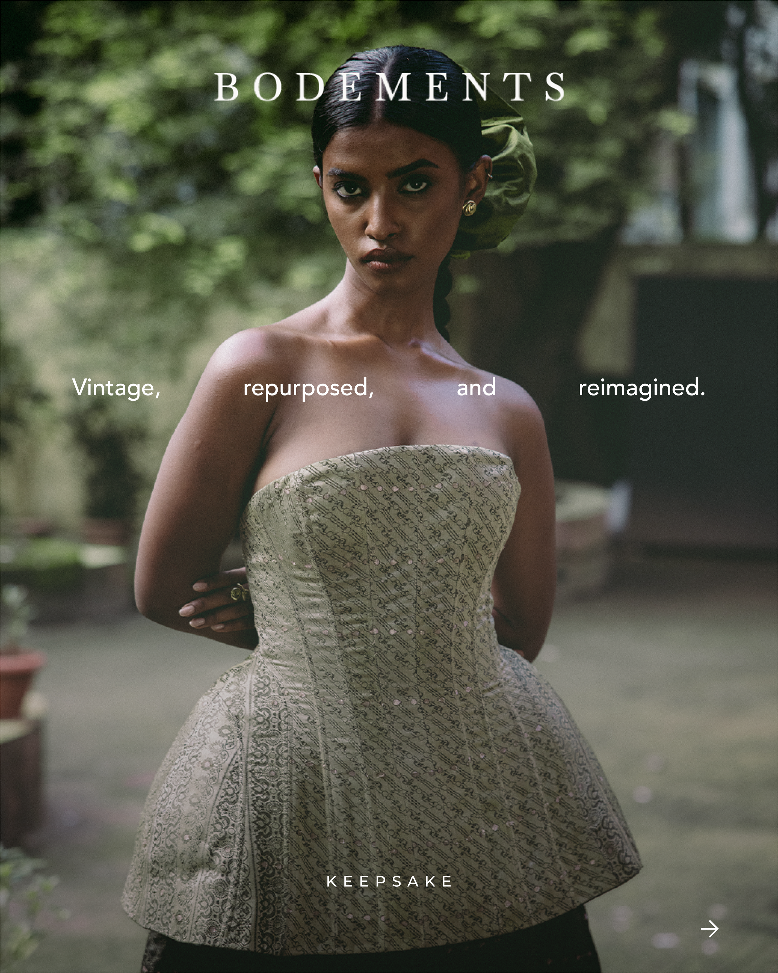 A woman wearing an elegant strapless dress with a patterned fabric stands outdoors with a blurred background of trees and plants.