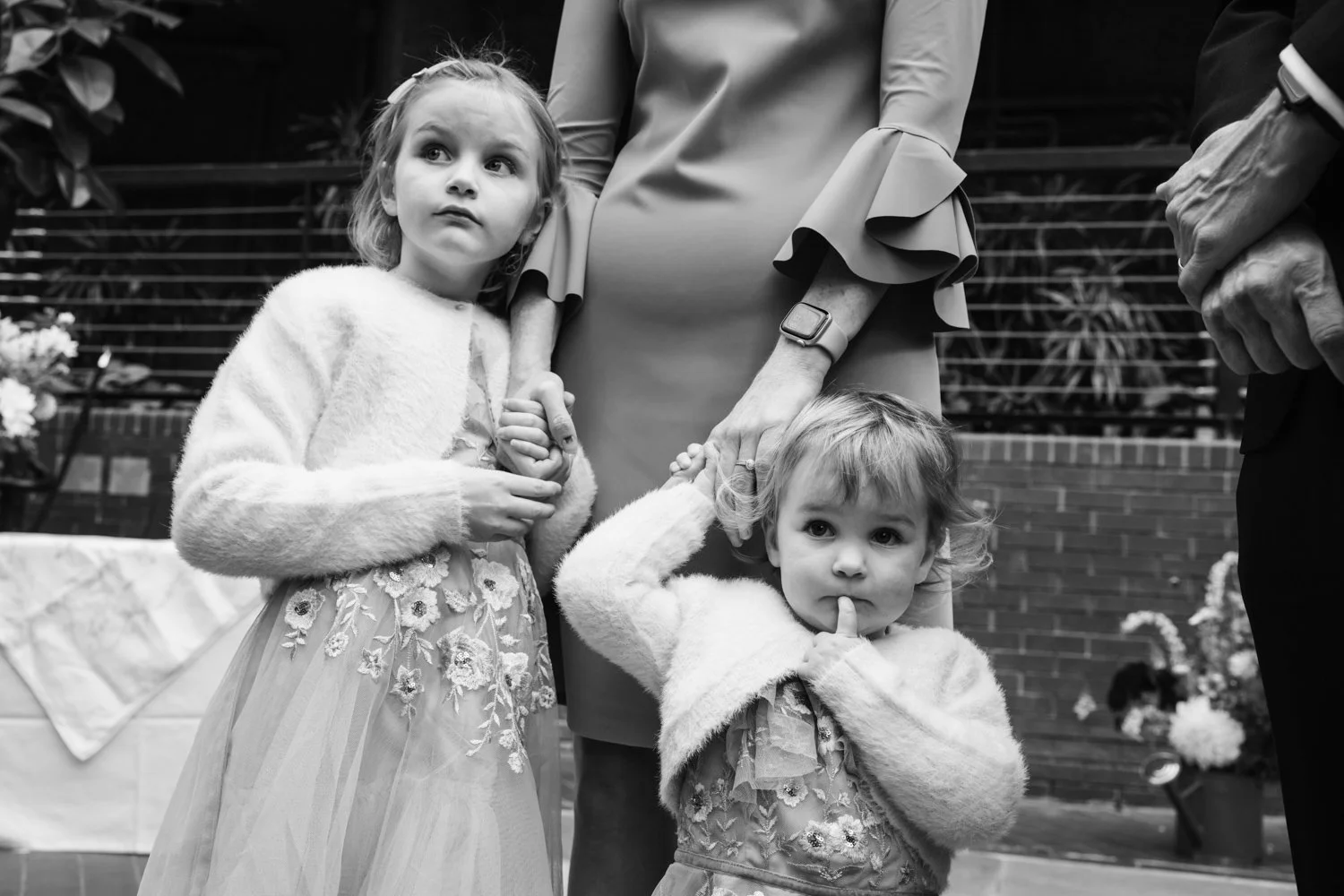 Two little girls holding hands with their mother and looking on at the crowd.