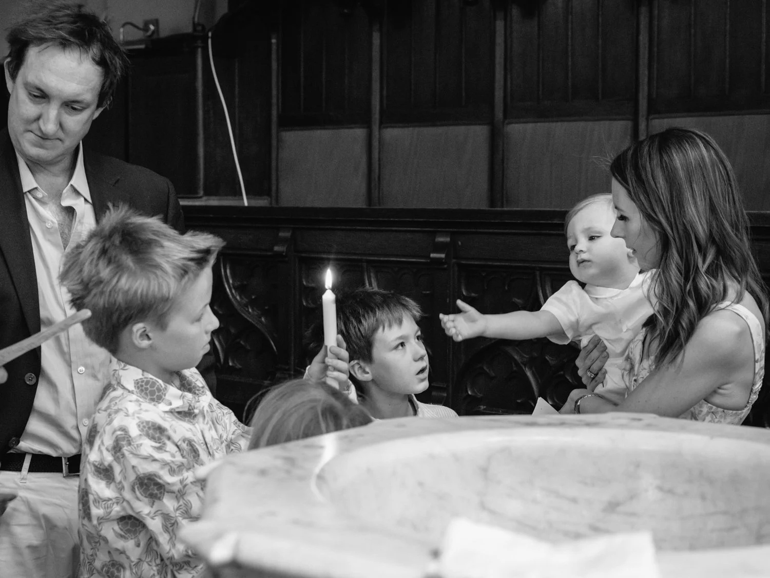 Baby brother reaches out from his mother's arms to take the lit candle