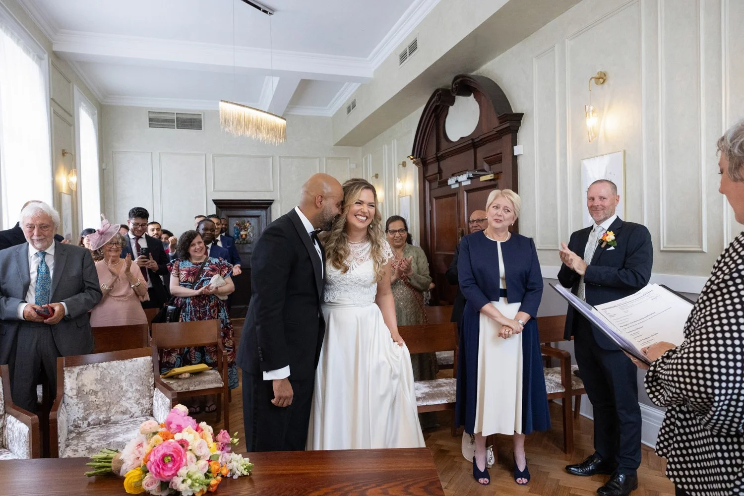 Bride and Groom with the groom leaning affectionately into the bride with parents weeping either side in the Brydon Room Chelsea Town Hall