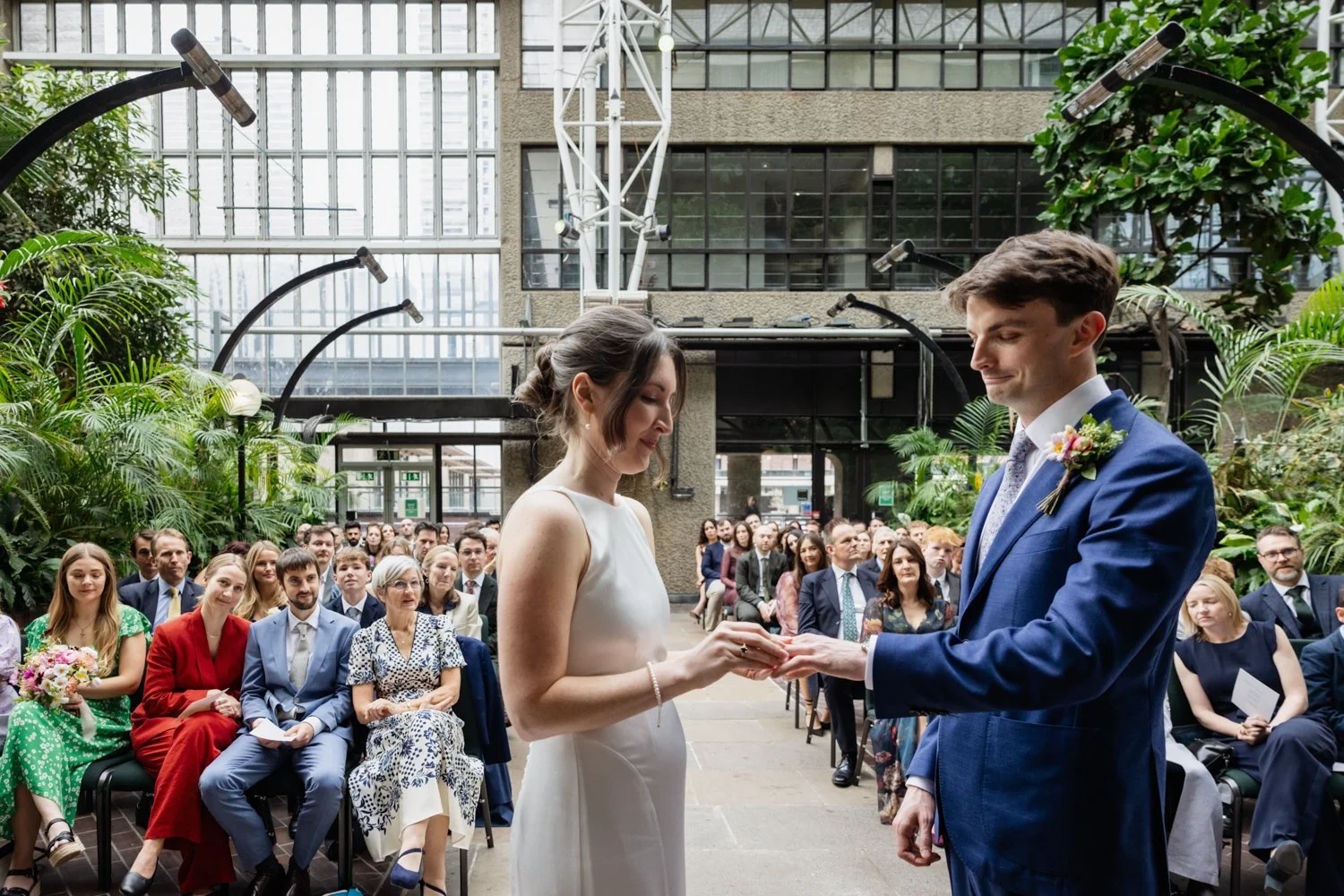 Bride putting ring on groom close up at the Barbican conservatory