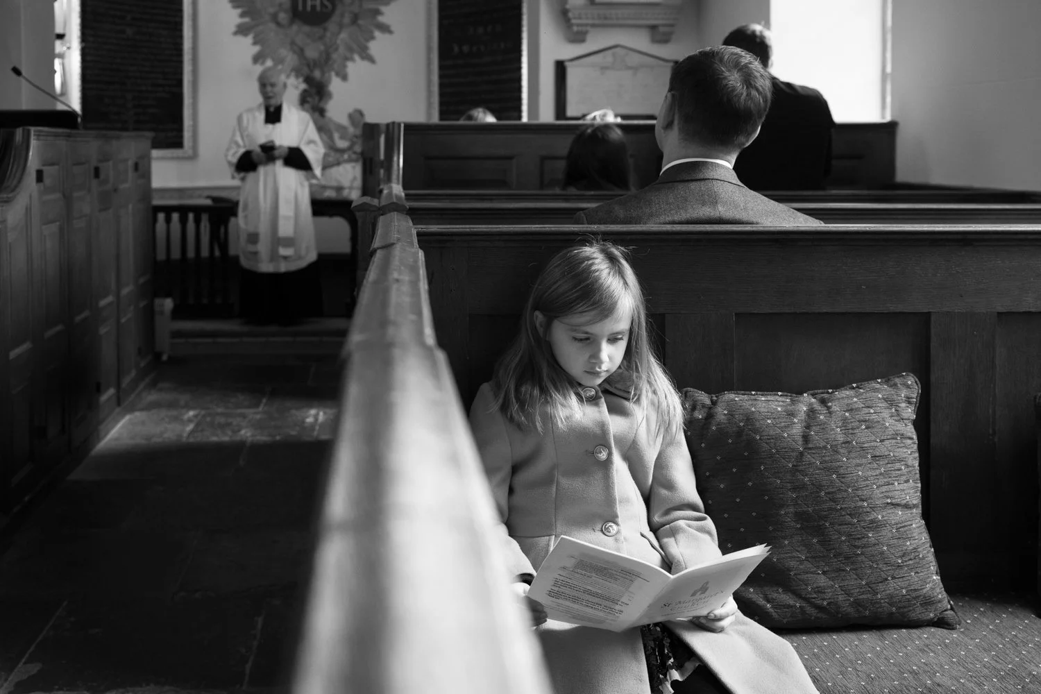 Young girl studying the order of service in a reversed pew at Babington House chapel