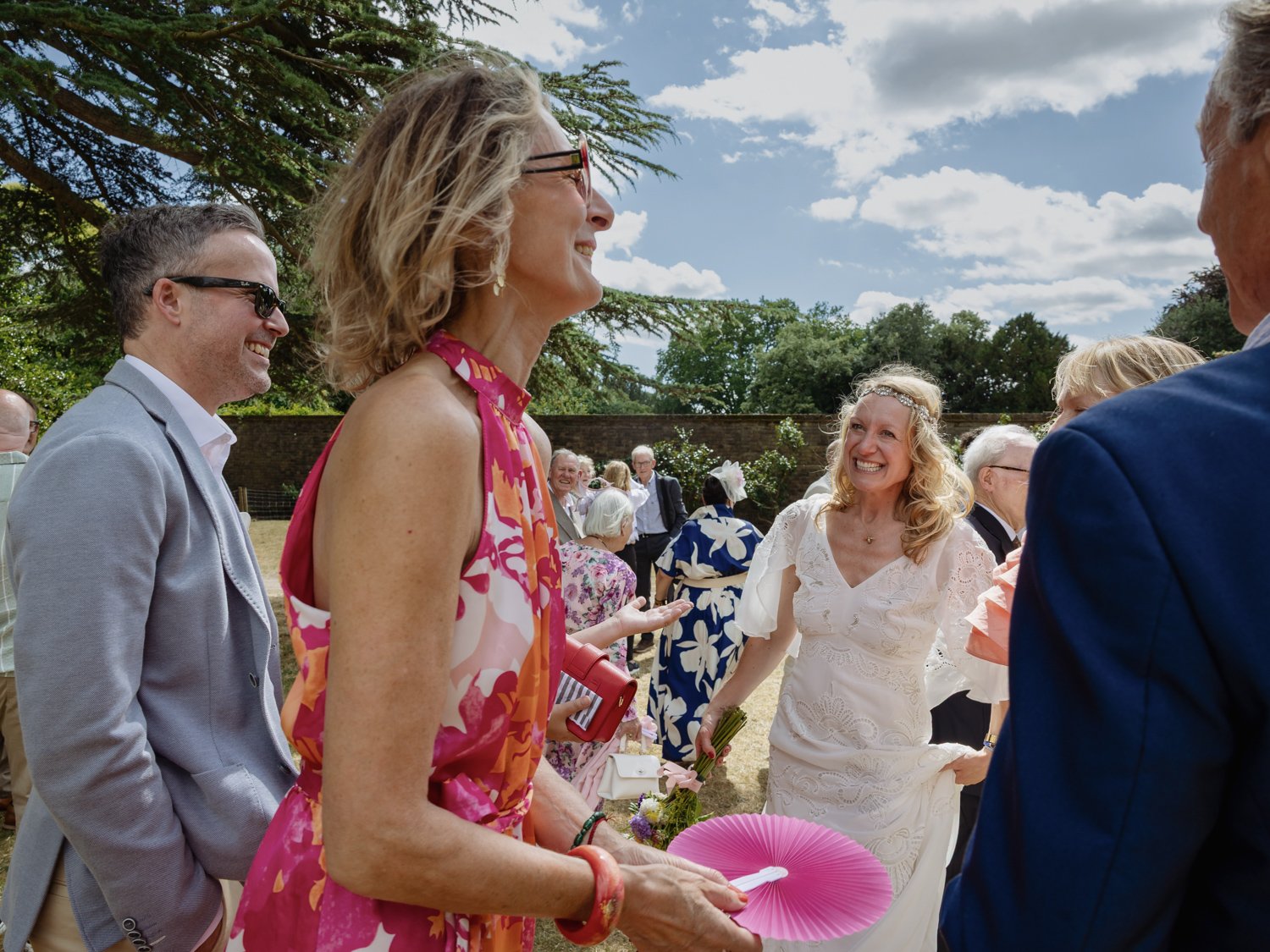 Bride with wedding guest with pink dress and pink fan.
