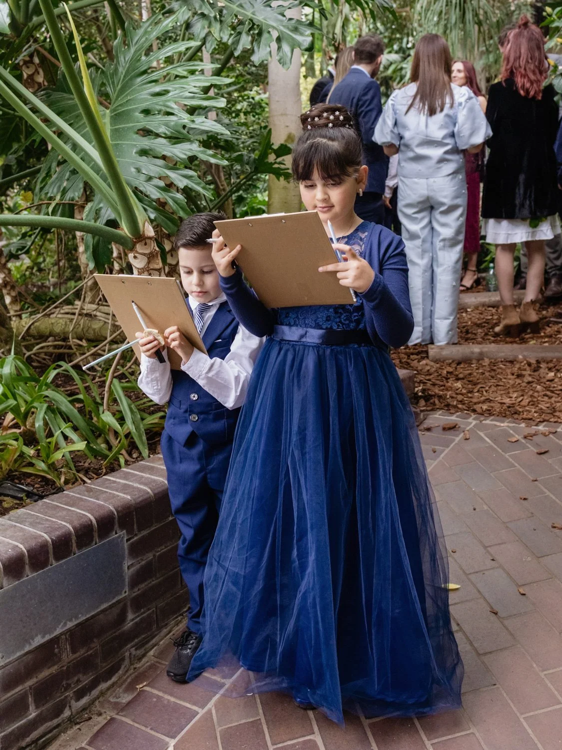 Two children dressed in blue young boy and older girl with clipboards studying a Treasure Hunt quiz during the reception.