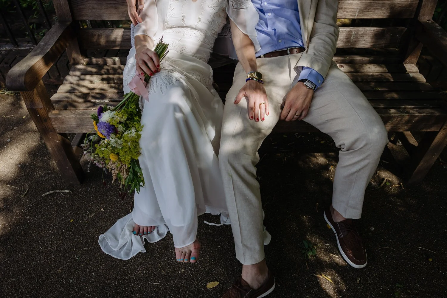 Detail of Bride and groom seated on bench showing her bare feet and her hand with wedding ring.