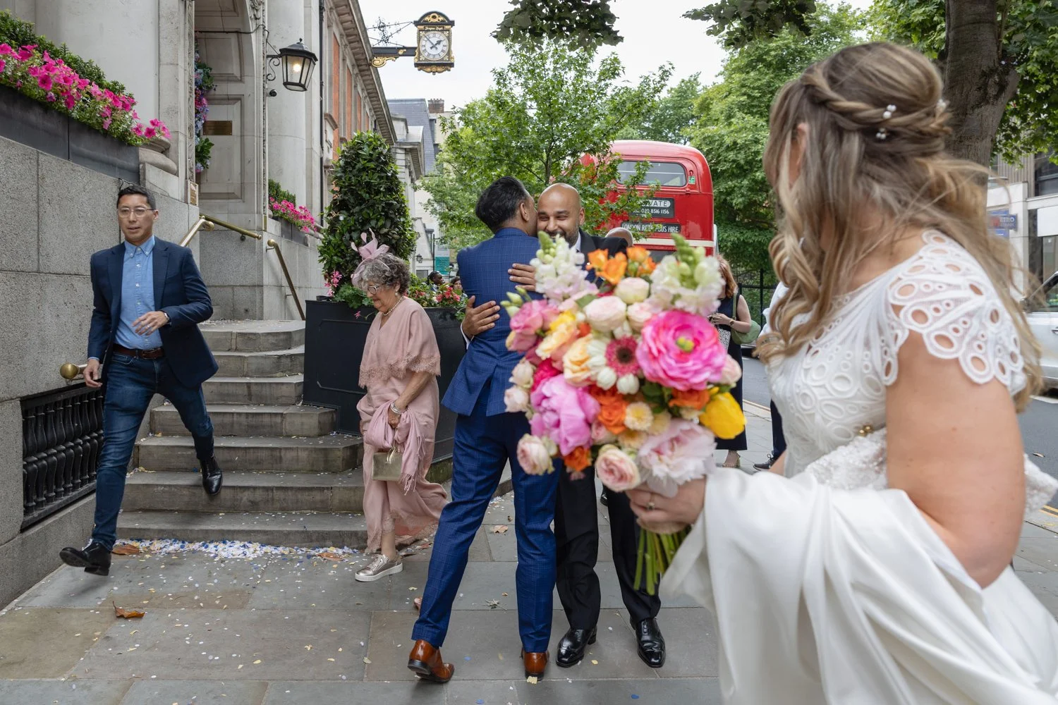 bride and groom hugging guests with route master bus in background