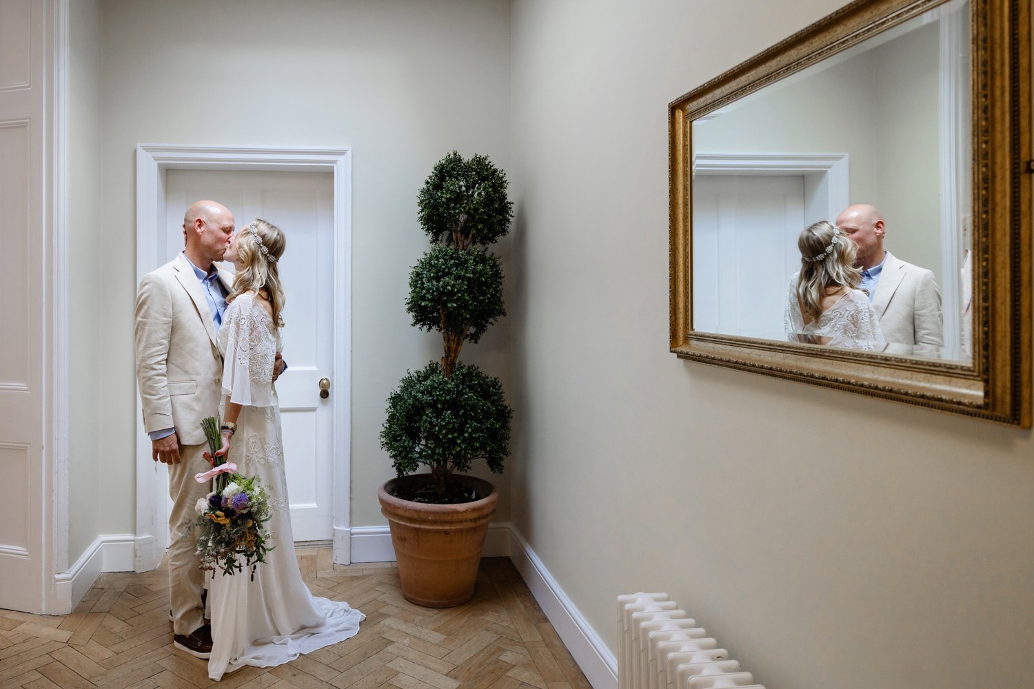 Bride and Groom first married kiss with their reflection on the right  hand side in a mirror.