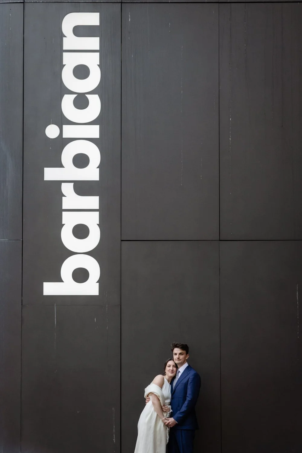 Bride and Groom portrait in front of wall at Barbican with the lettering Barbican on it.