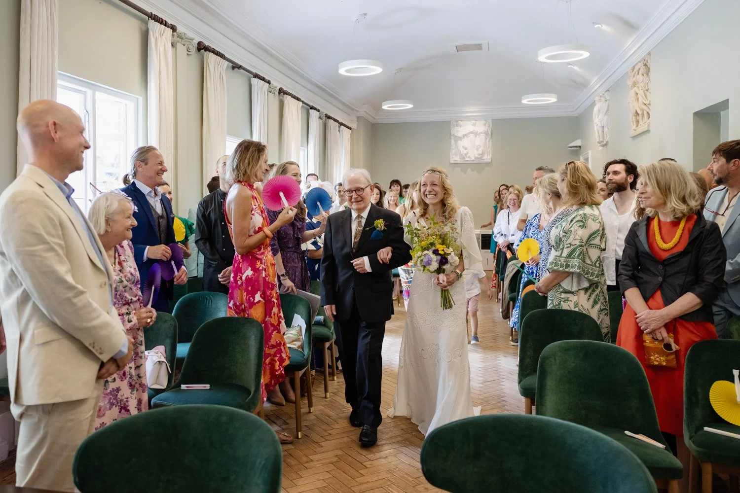 Father and bride arrive at the top of the aisle with guests and groom smiling.