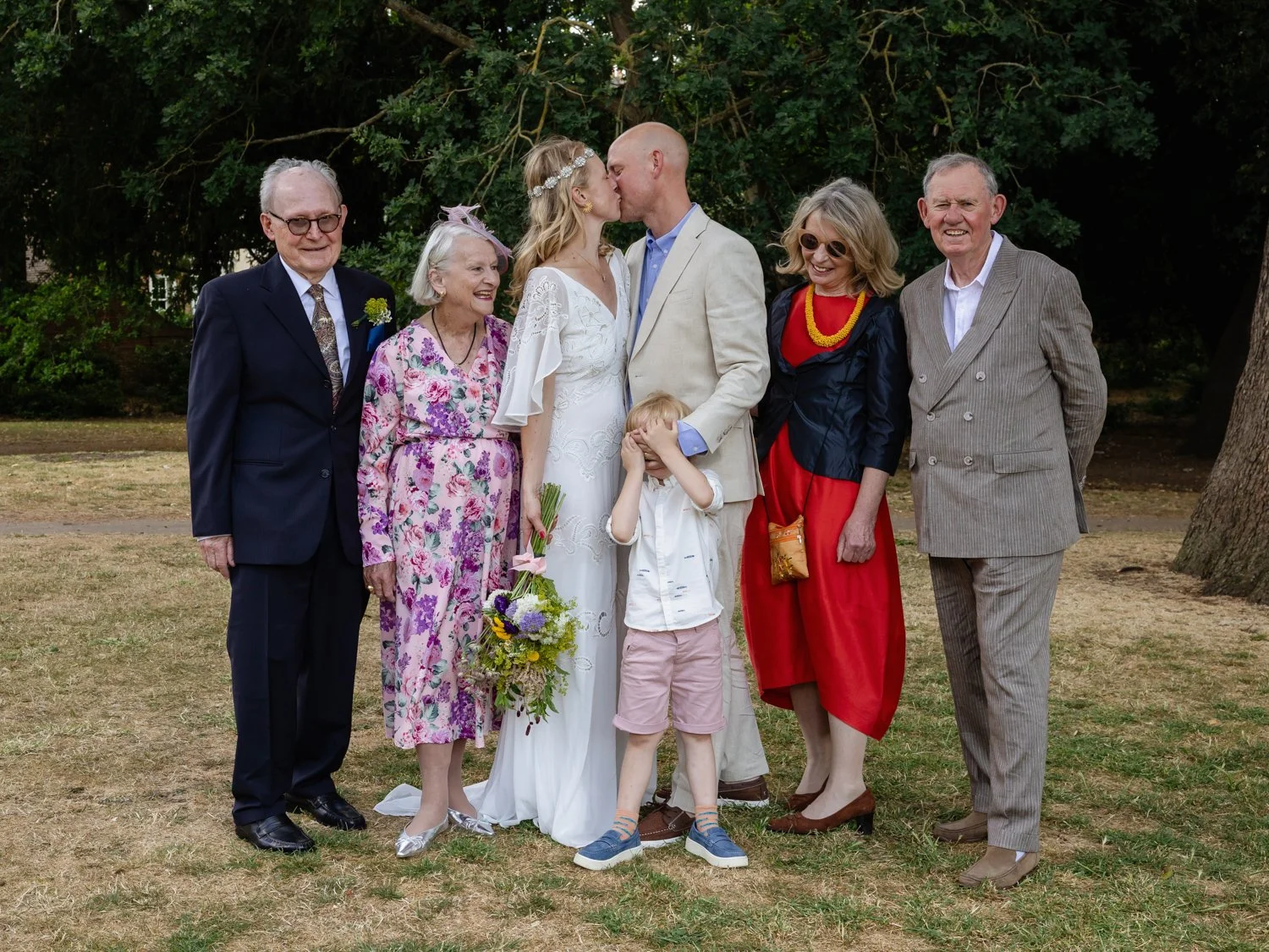Group photo with bride and groom kissing and the groom covering his son's eyes.