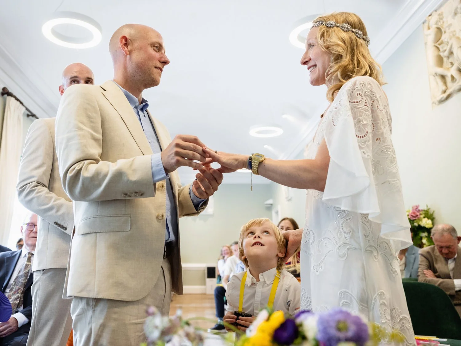 Groom places the ring on bride's finger as their little boy looks on.