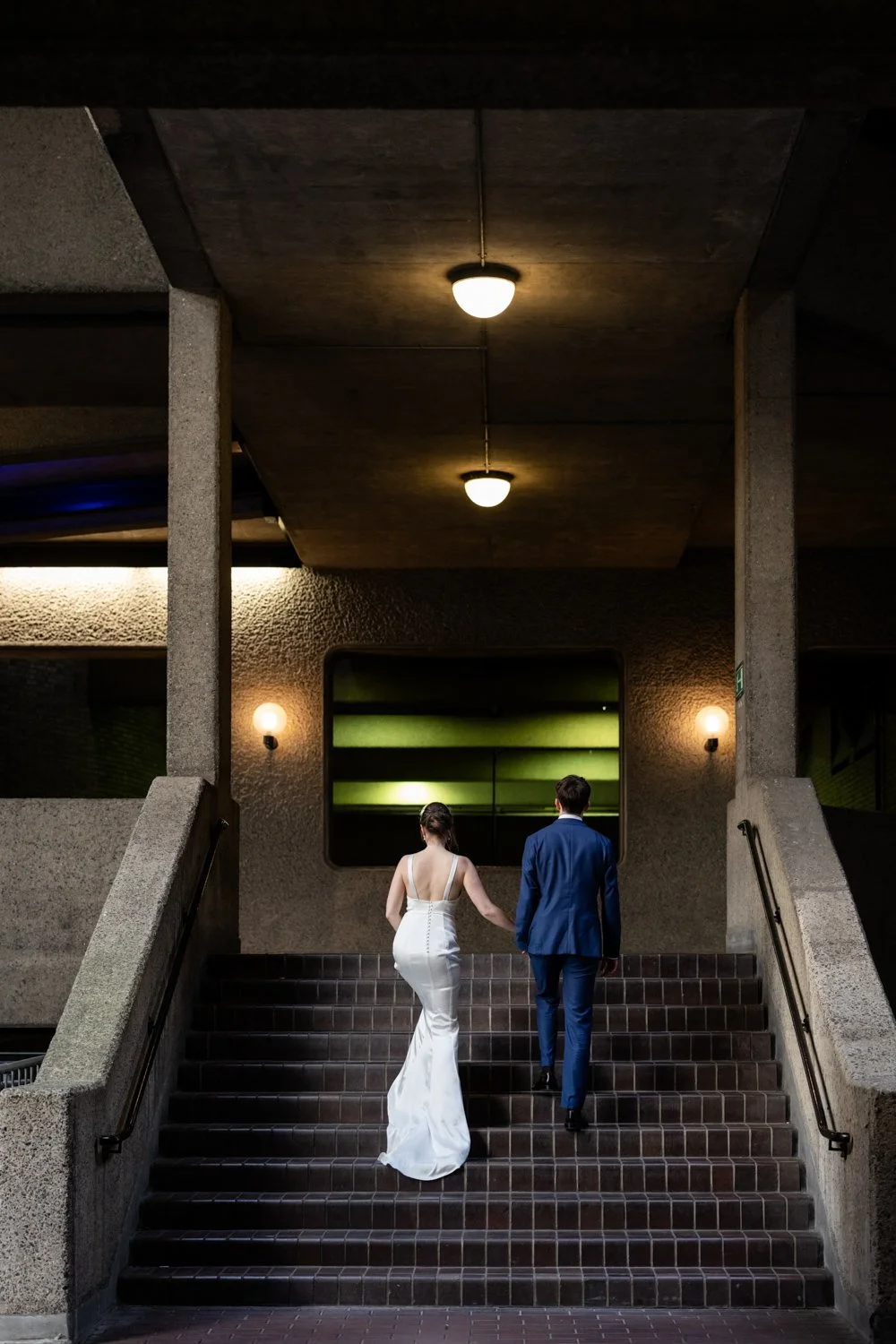 Bride and Groom climbing the steps in a darkly lit part of the Barbican complex